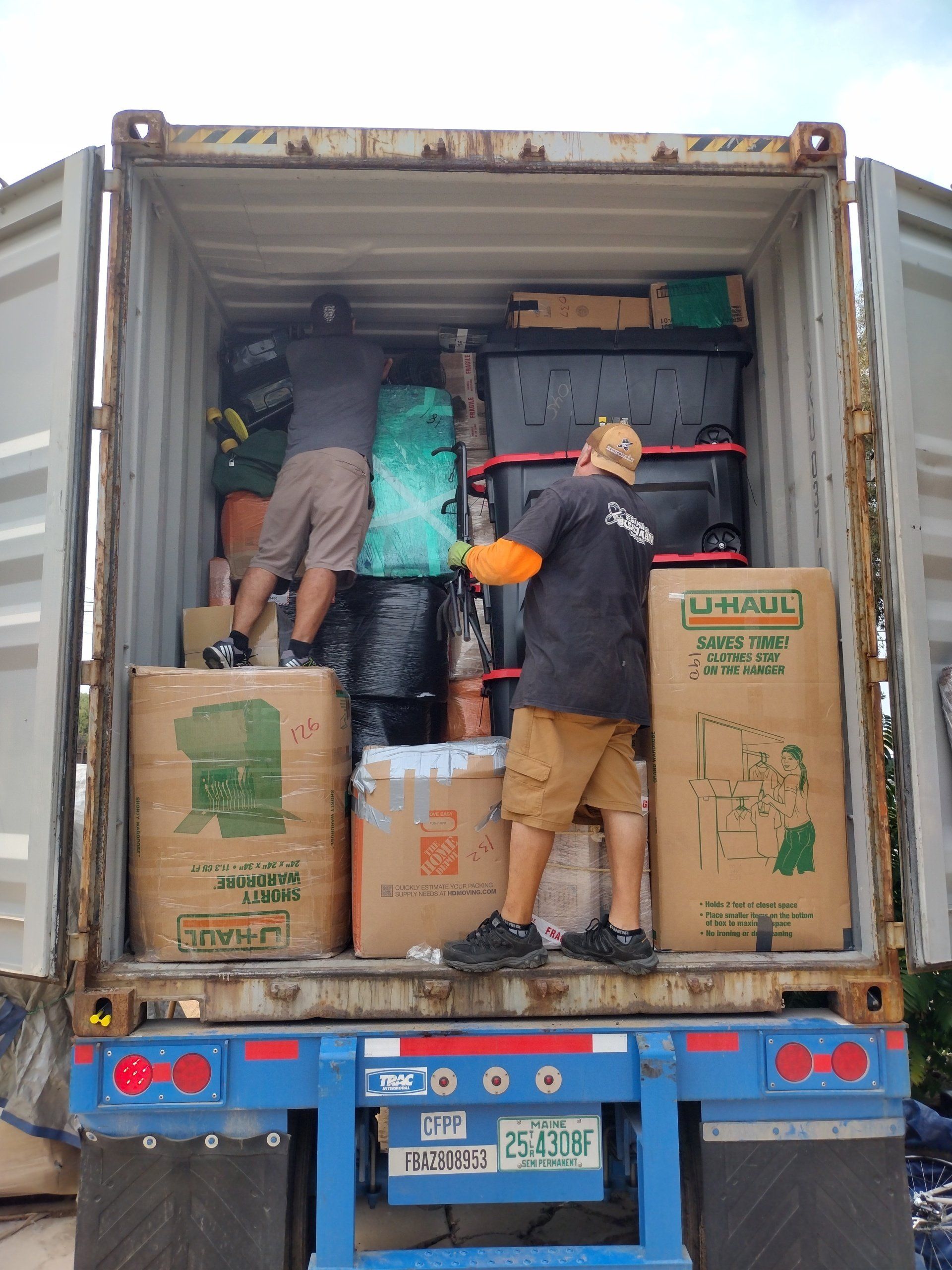 Two people loading boxes and items into a shipping container on a truck.