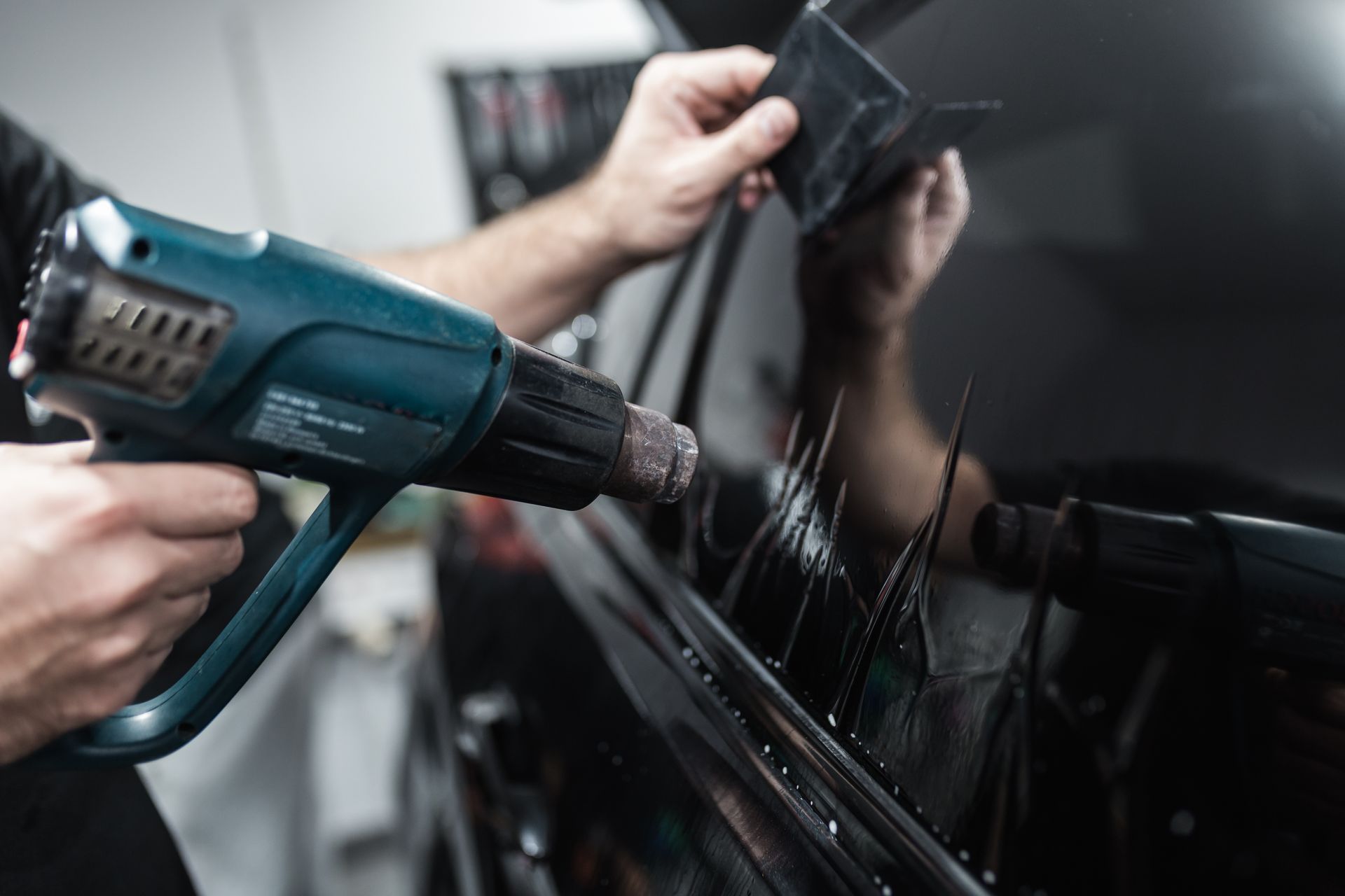 A person uses a heat gun to apply window tint to a car's rear windshield.