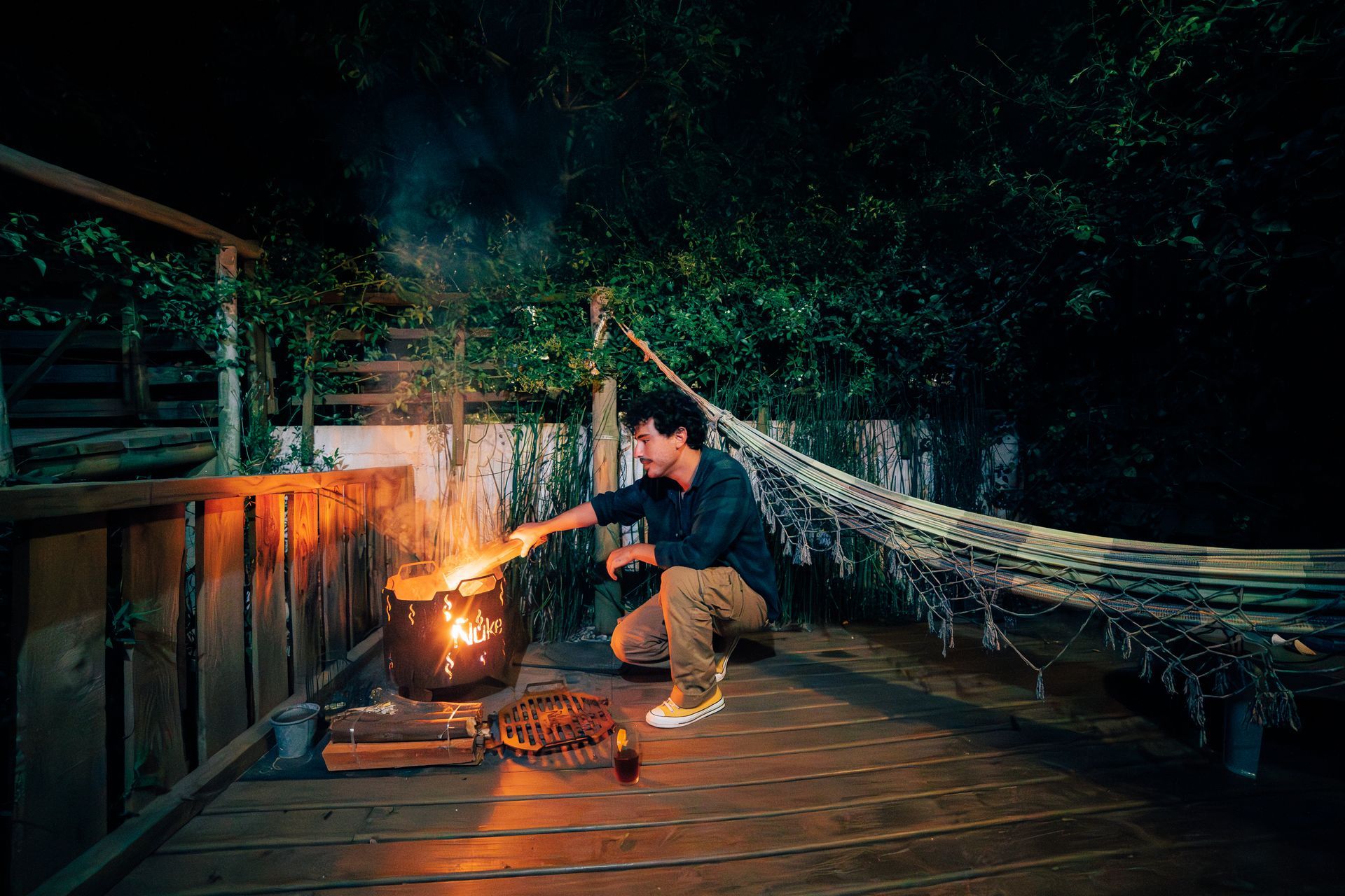 A man is cooking over a fire on a deck at night.