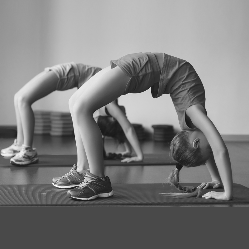 Two young girls are doing a handstand on a yoga mat