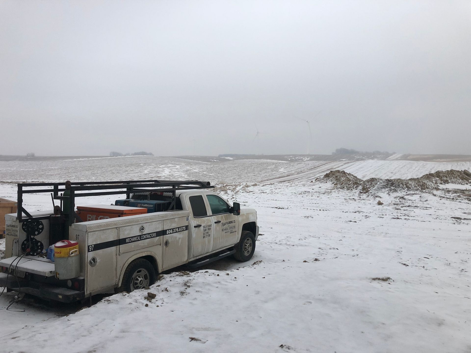 White work truck in a snowy field. Gray sky.
