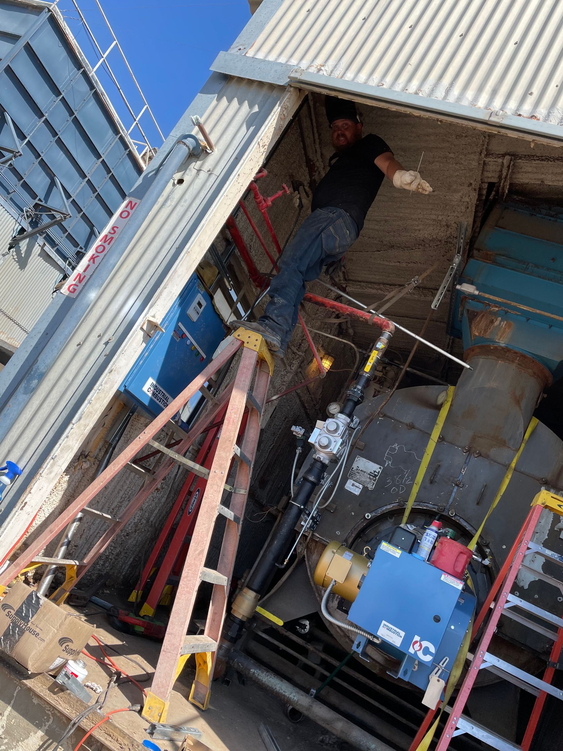 Man on a ladder working on machinery inside a building.