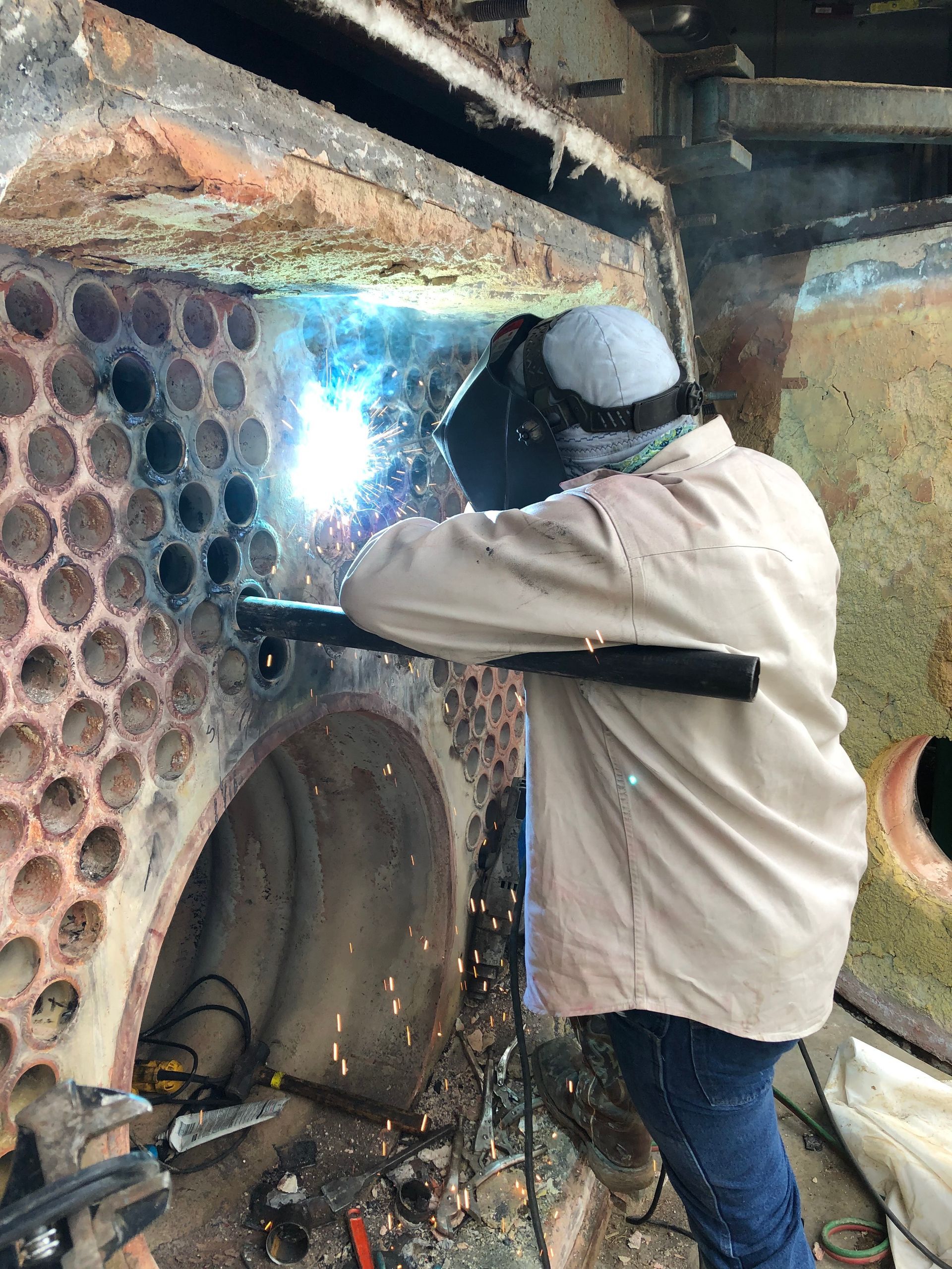 Welder in protective gear, welding inside a large industrial structure, sparks flying.