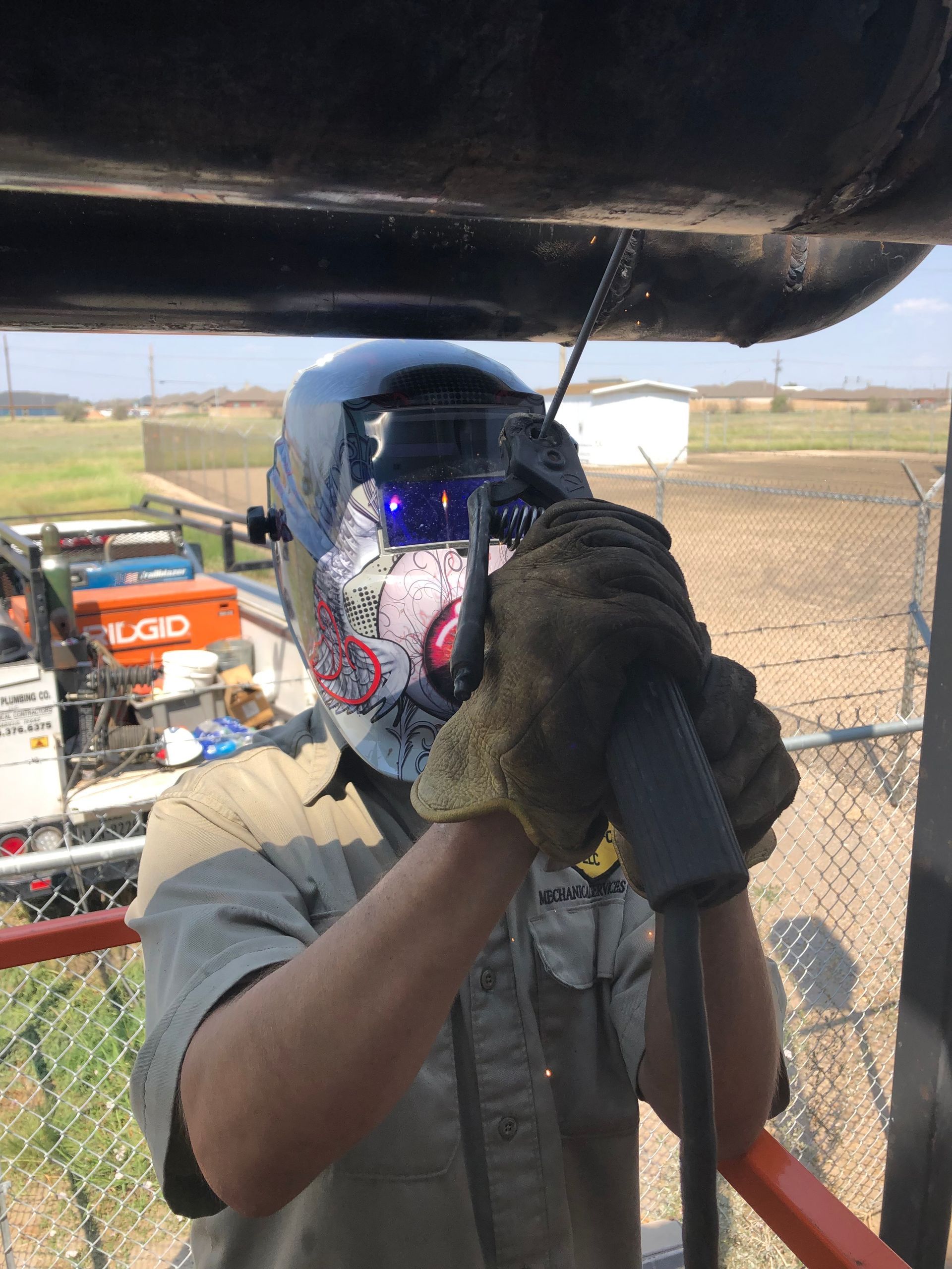 Welder in protective gear welding black pipe outdoors.