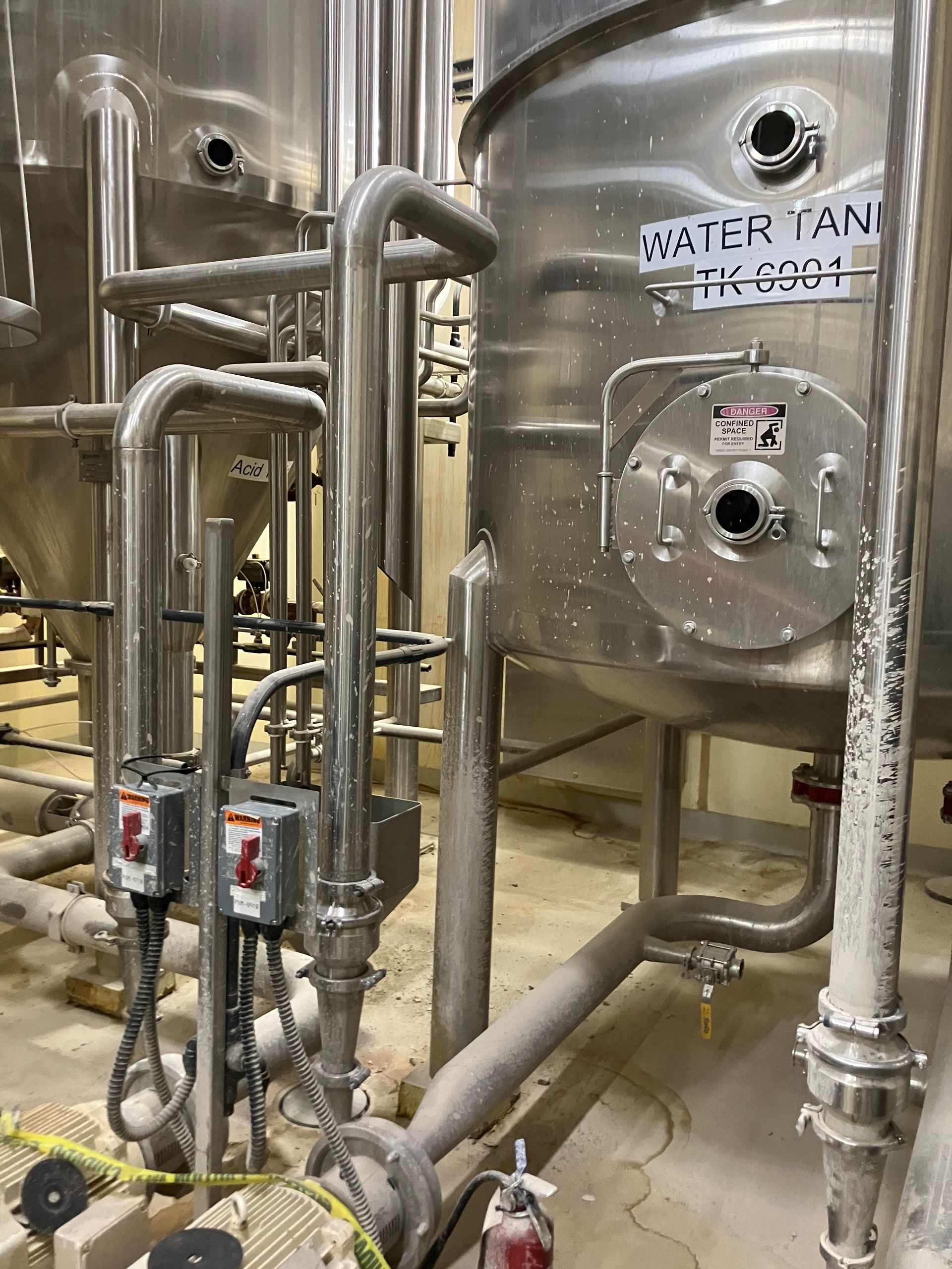 Stainless steel industrial equipment, pipes, and water tank in a factory setting.