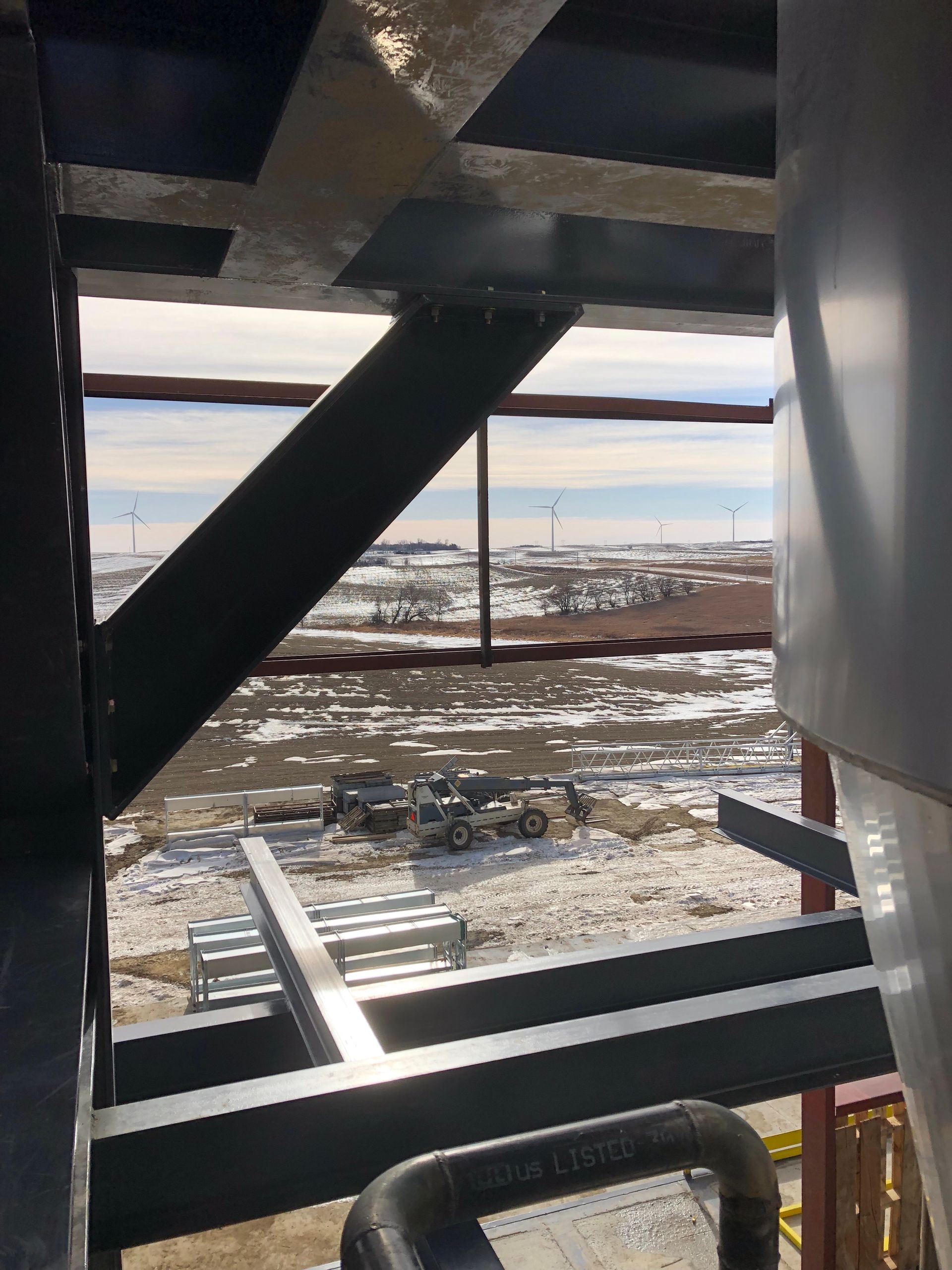 Steel beams frame a distant landscape with construction equipment and wind turbines.