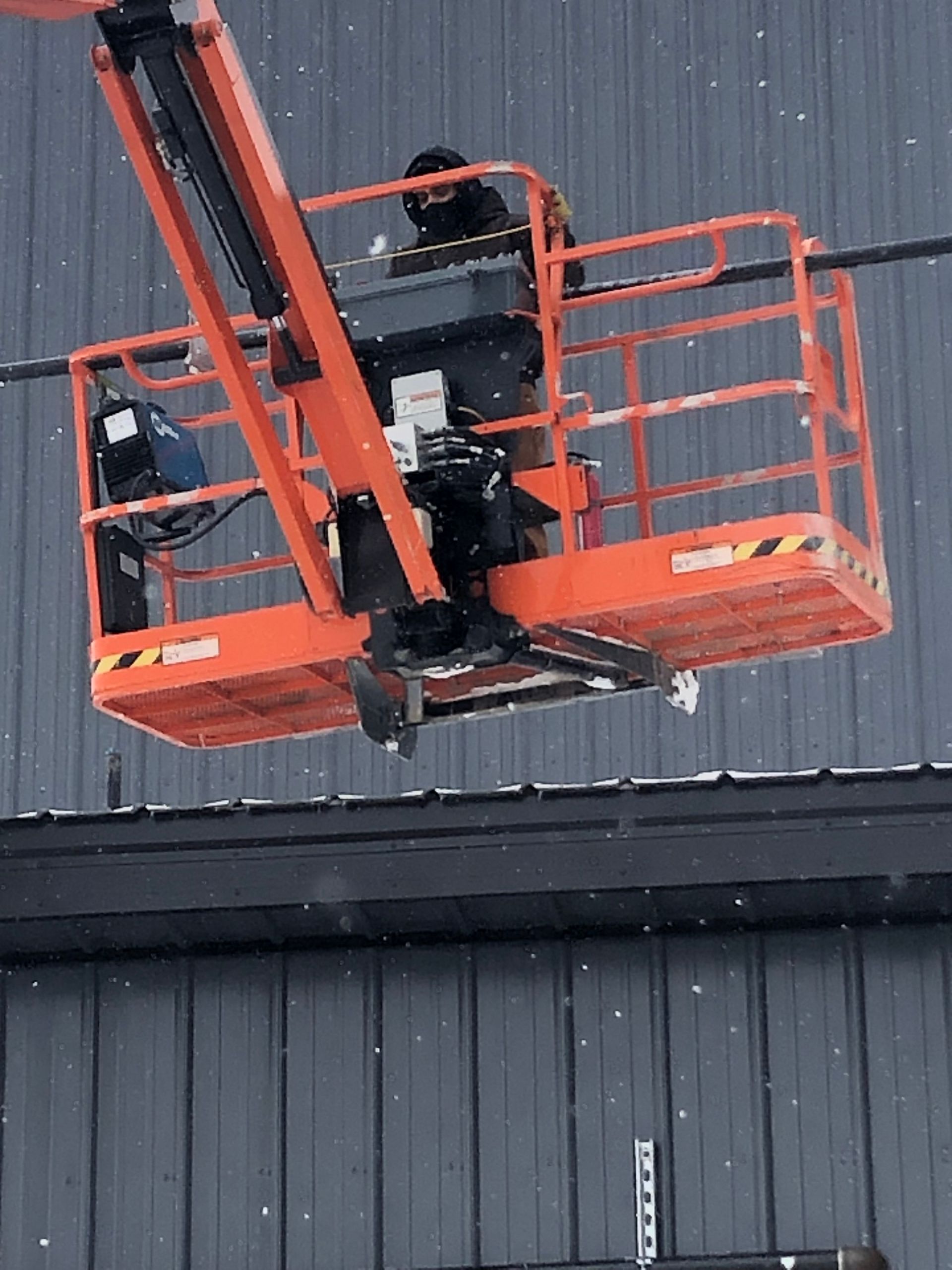 Person in an orange lift basket working near a building with a gray exterior.