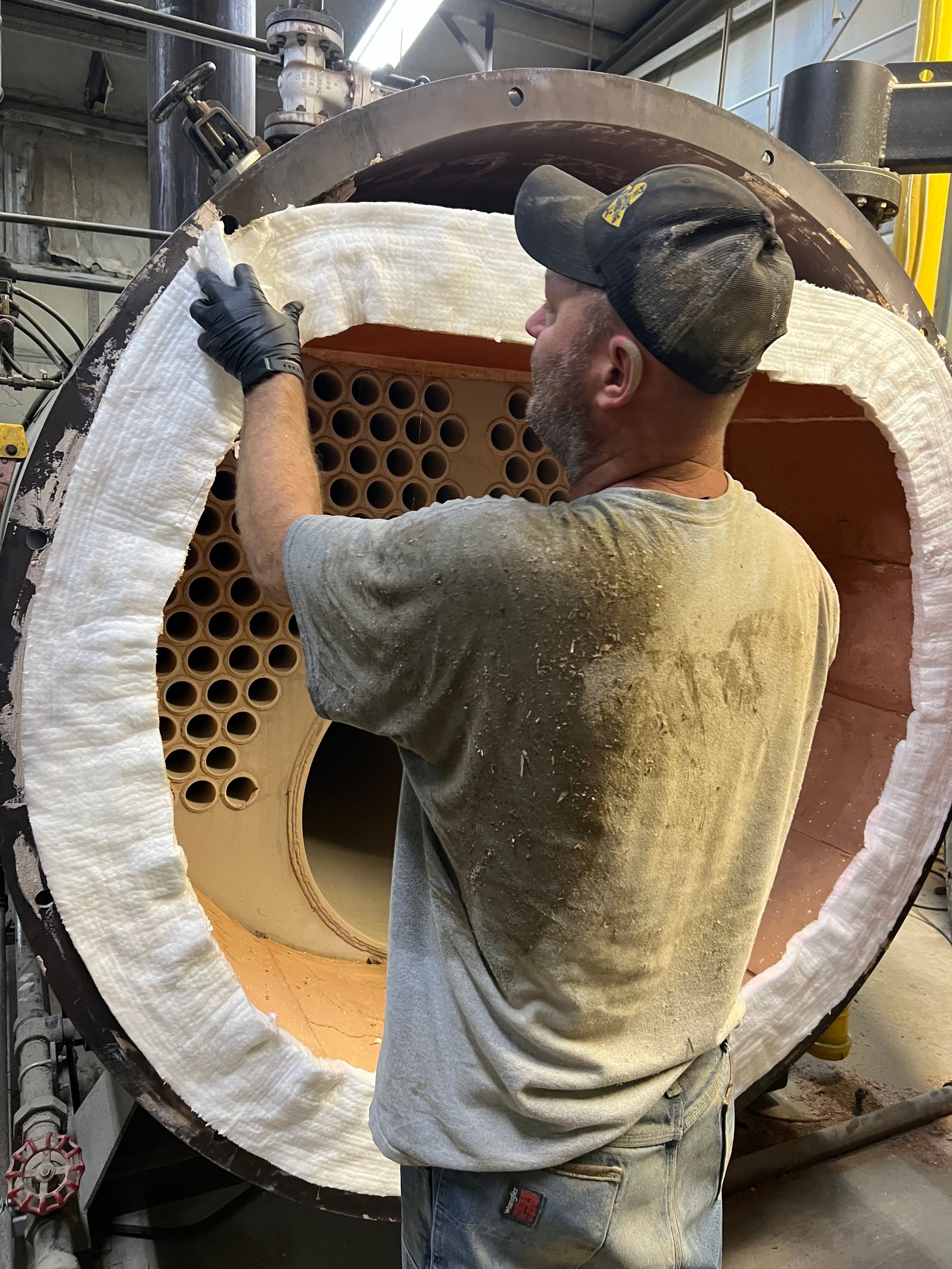 Man installing insulation inside a large industrial boiler.