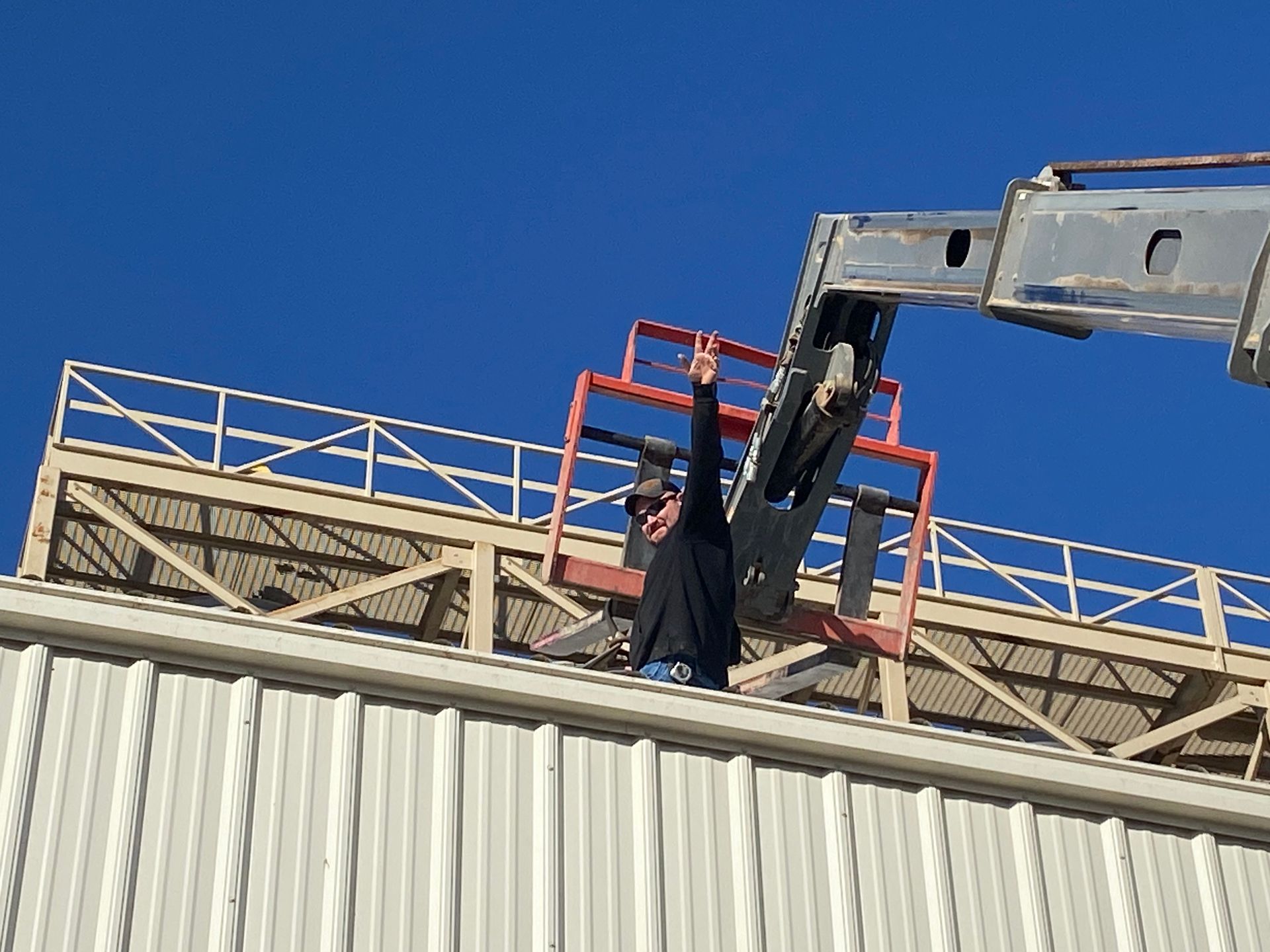 Person on a lift waving on a building's roof. Blue sky, industrial setting.
