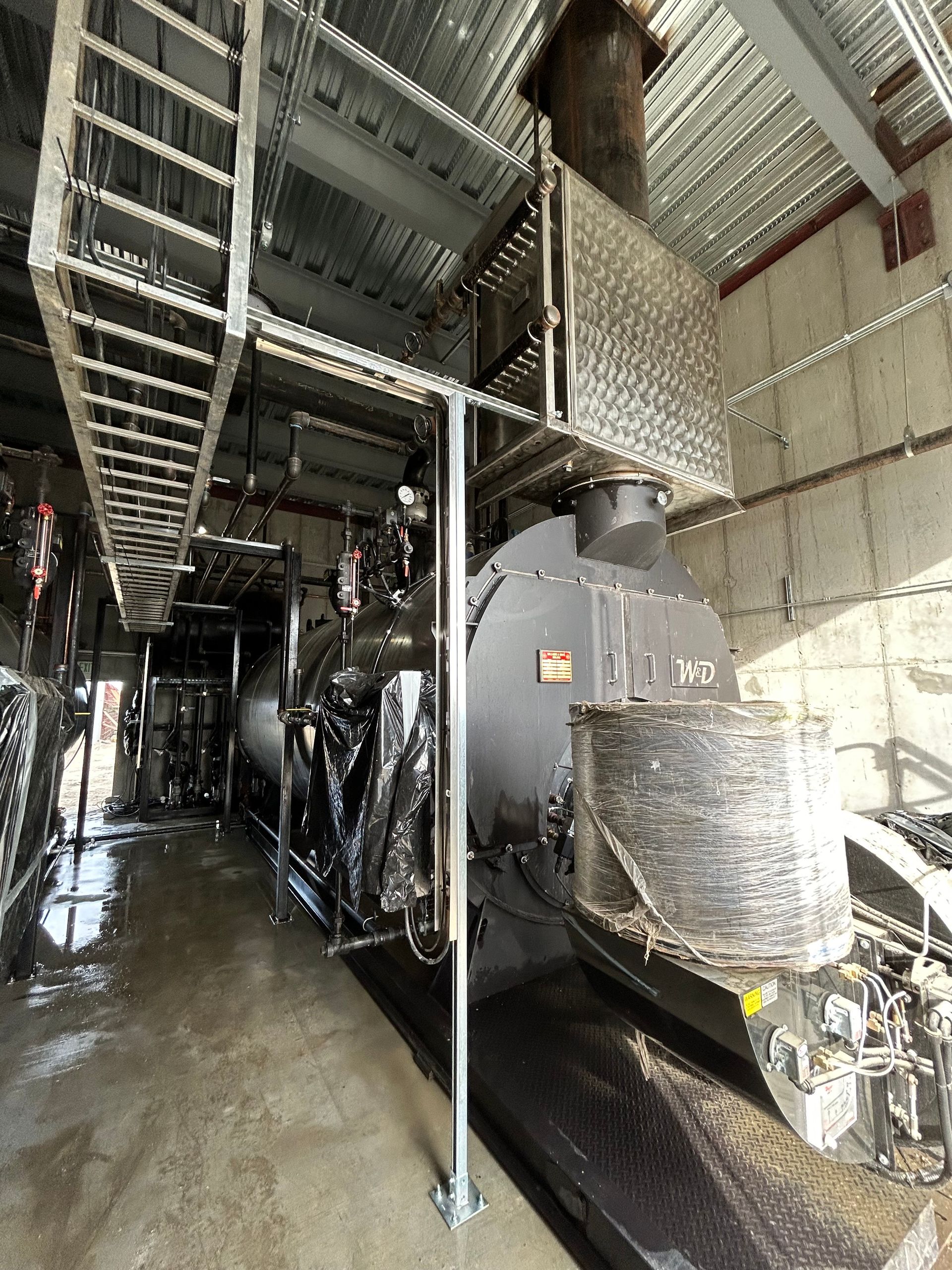 Black steam engine inside a building, with a ladder above.