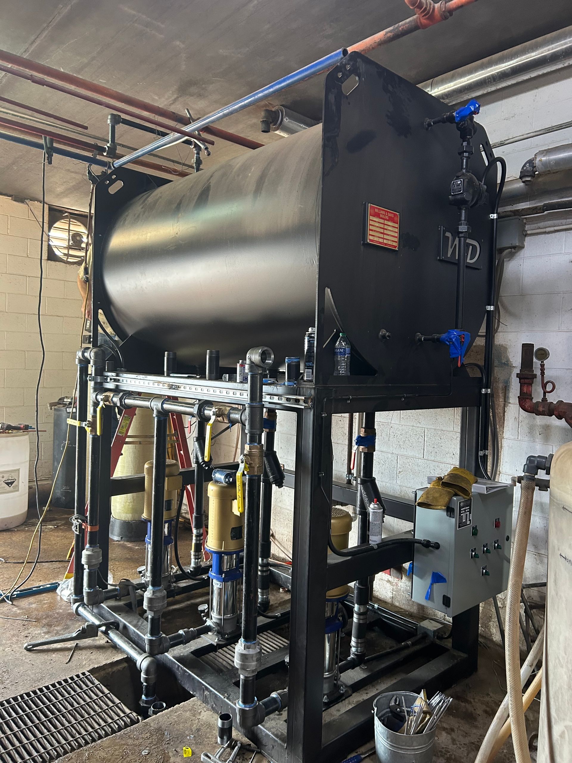 Large black industrial water tank with associated piping and equipment in a utility room.