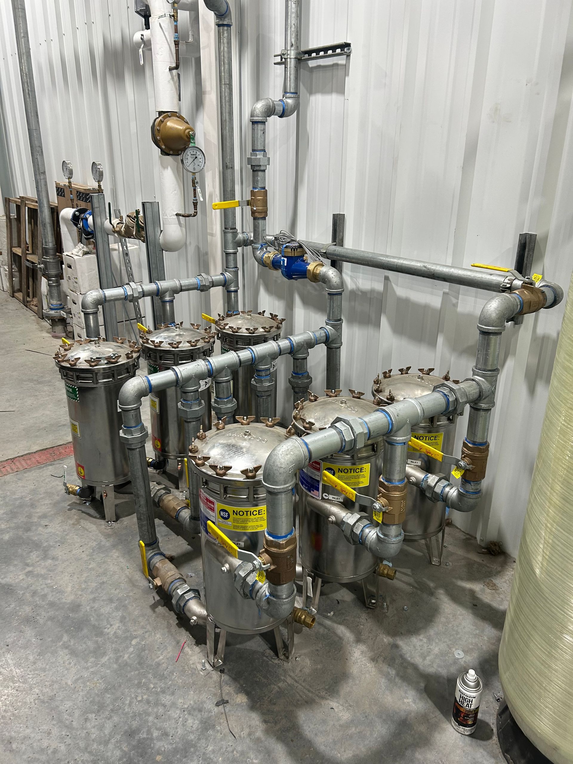 Industrial stainless steel filtration system with pipes, valves, and cylindrical filters in a factory setting.