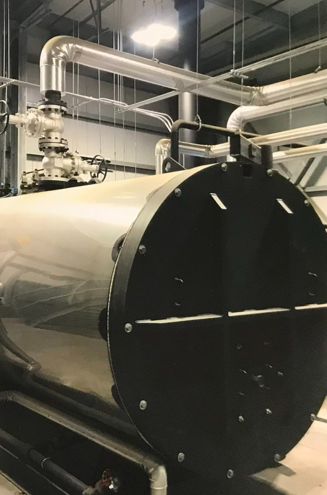 Large industrial tank with black end cap, silver piping, and metal supports.