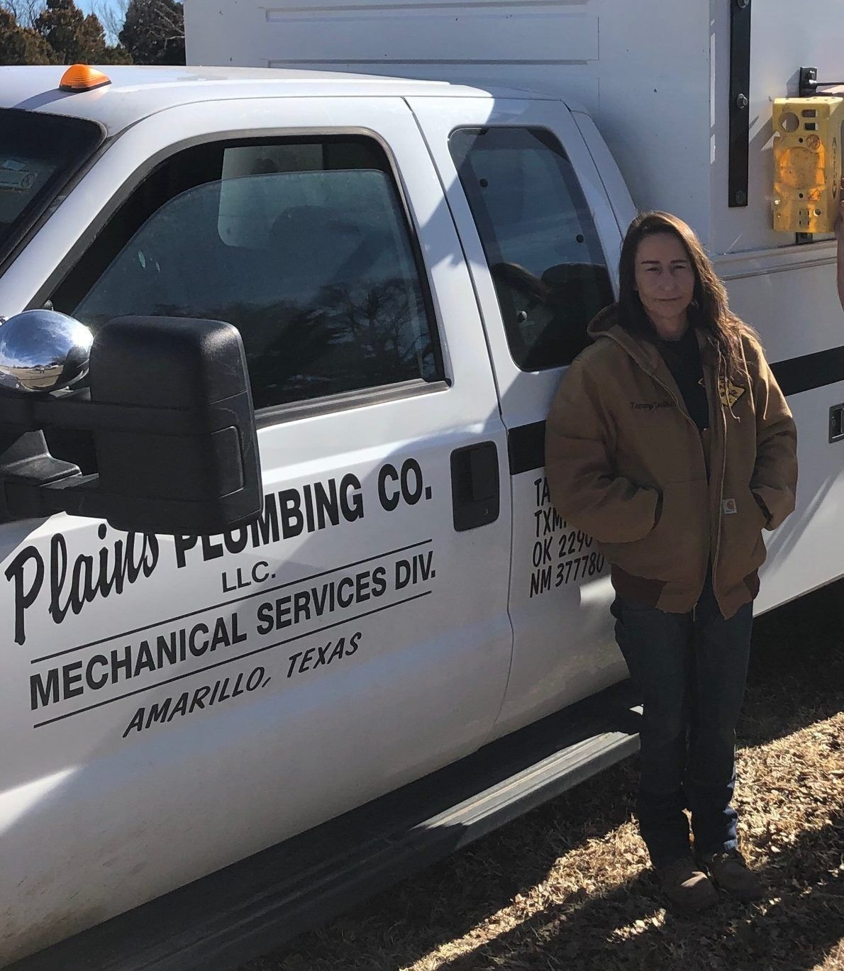 Woman in brown jacket stands by a white Plains Plumbing truck in Amarillo, Texas.