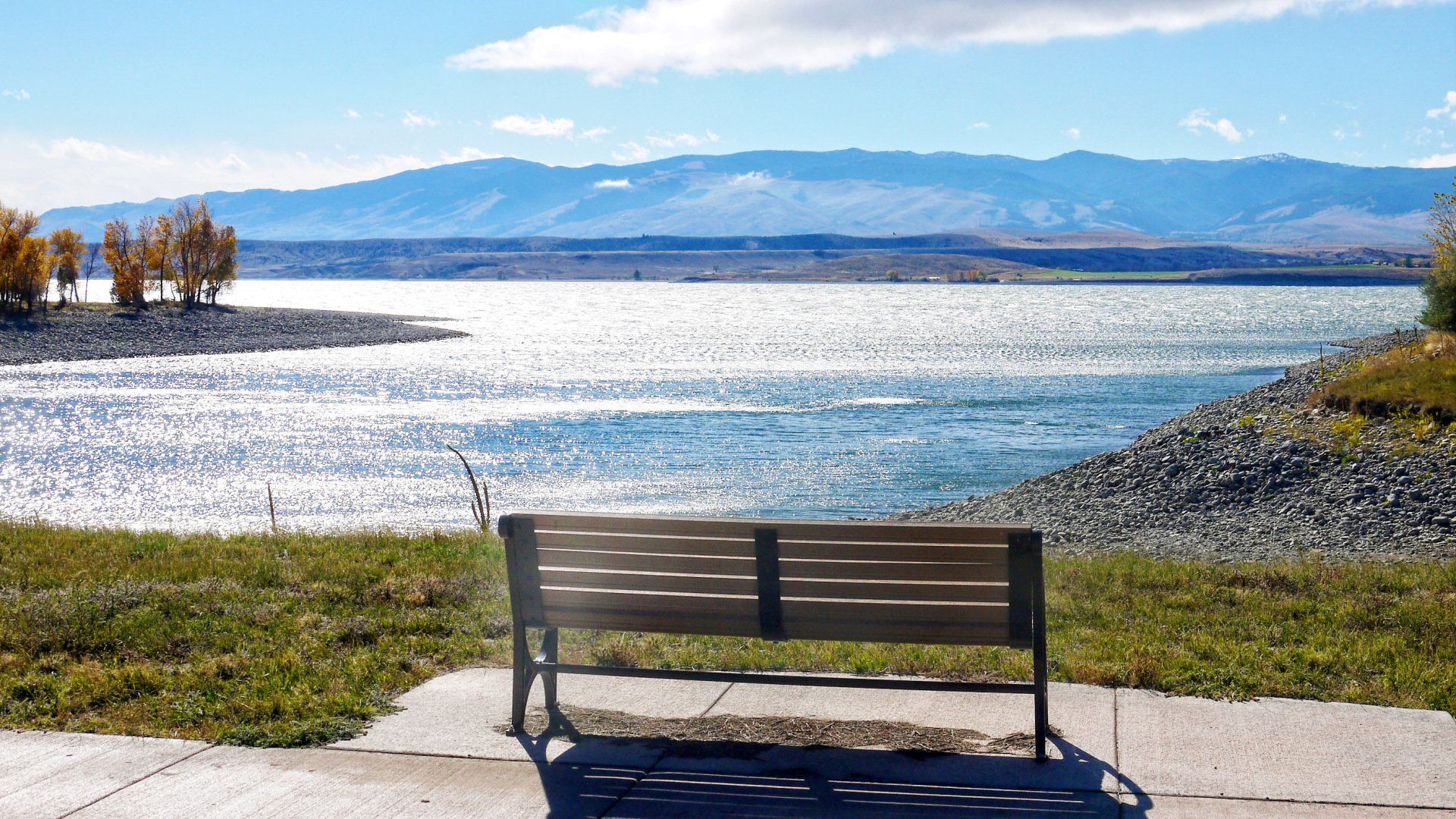 A wooden bench is sitting in front of a lake with mountains in the background.