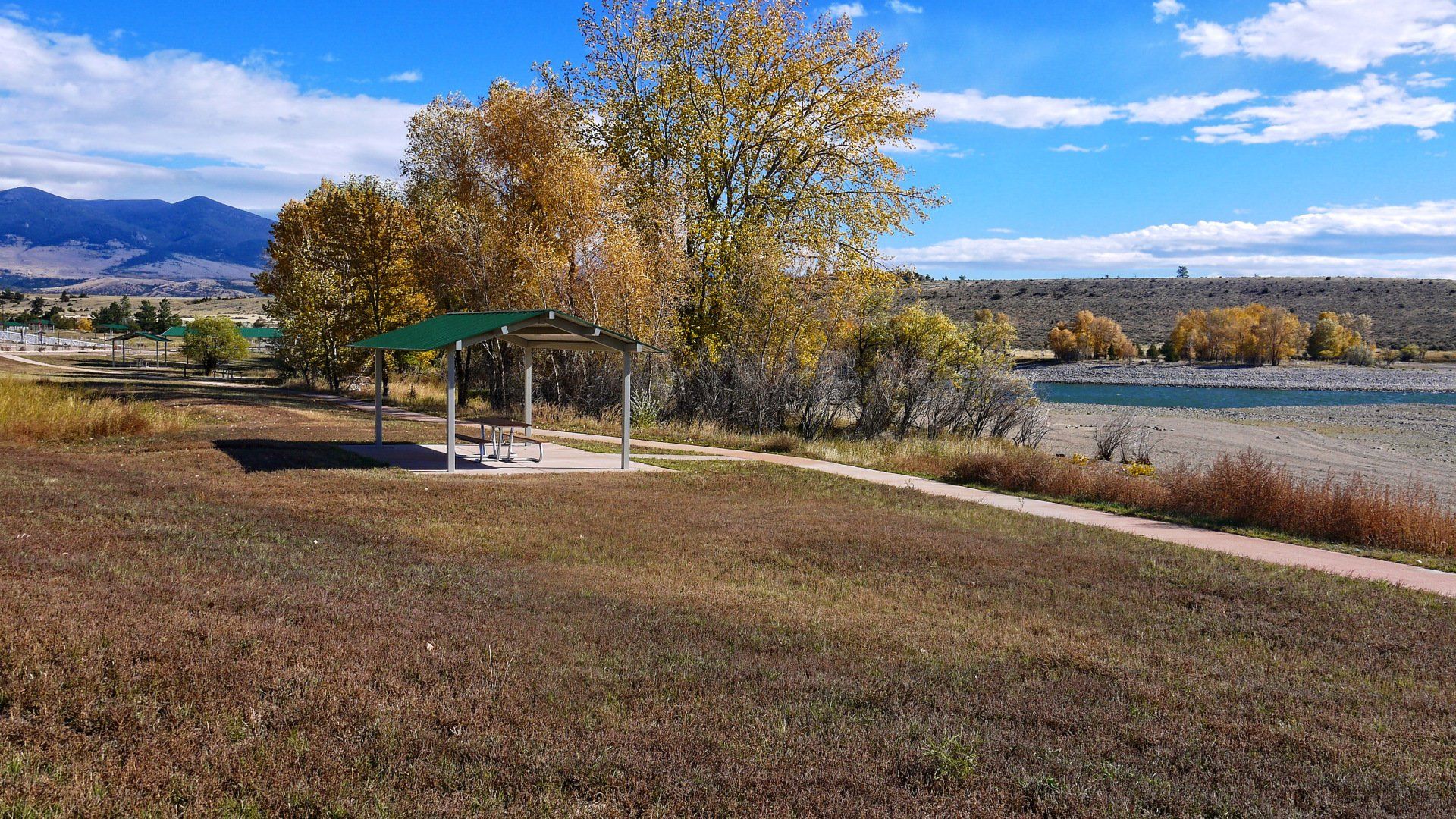 There is a picnic shelter in the middle of a field next to a lake.