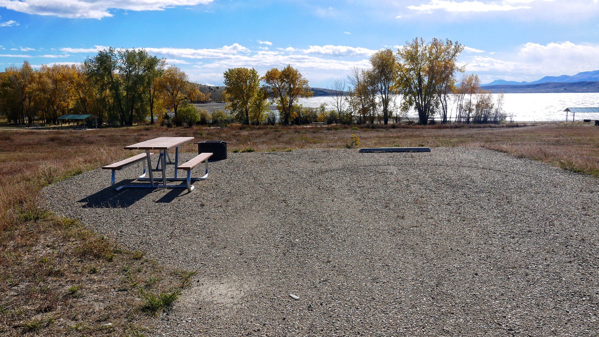 A picnic table in a gravel area with a lake in the background