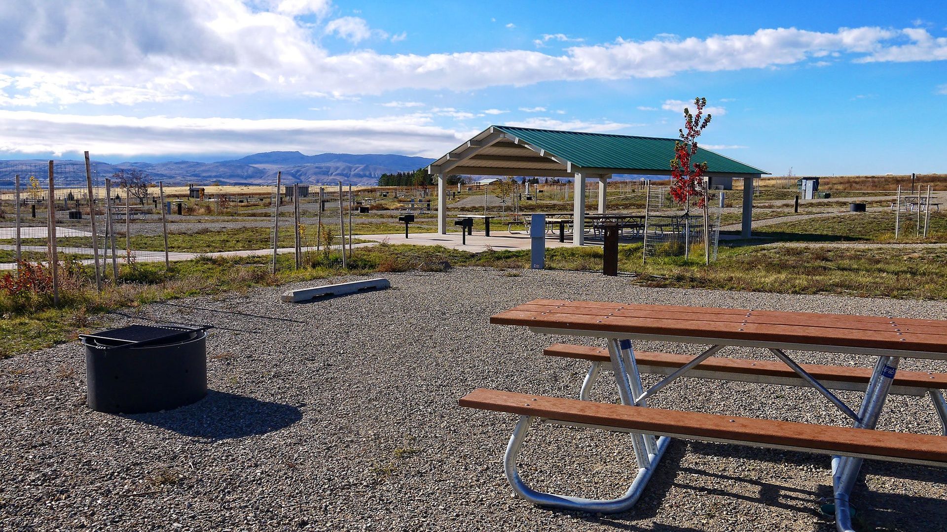 A picnic table and a fire pit in a gravel area.