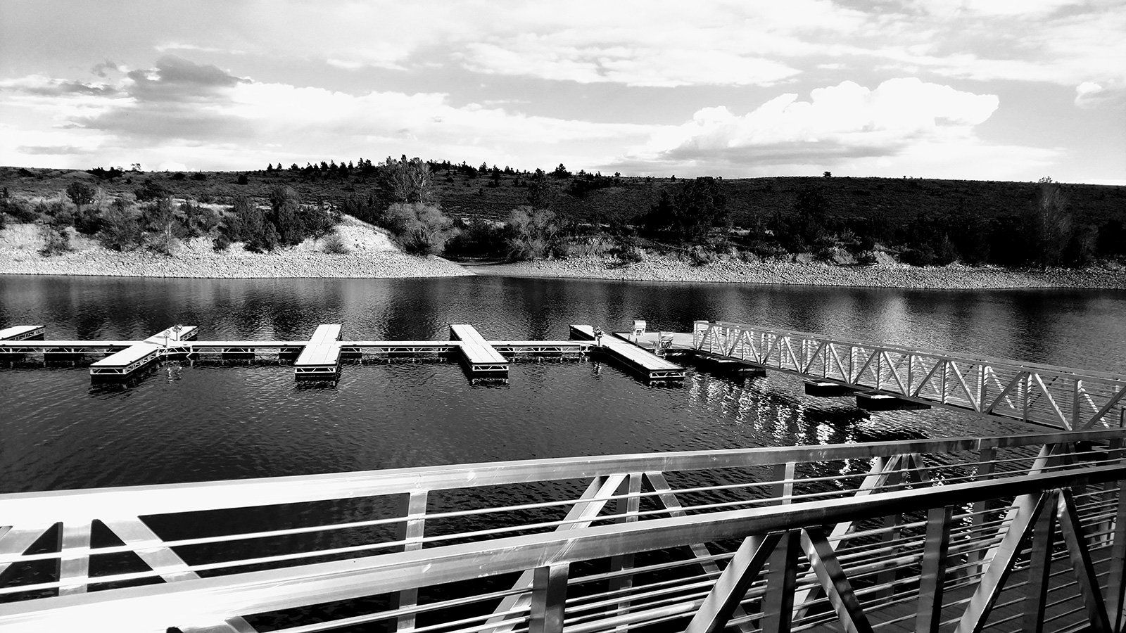 A black and white photo of a lake with a bridge in the foreground