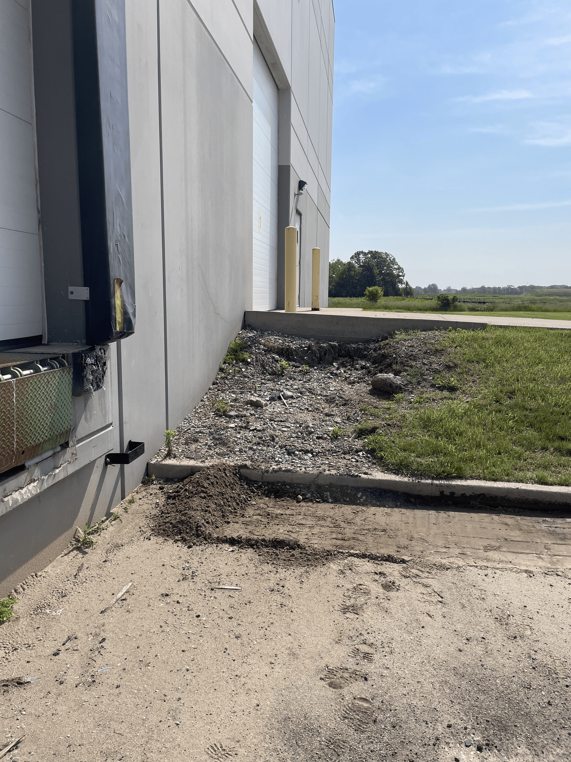 Exterior of a loading dock with a gravel ramp, concrete, and grass against a white building on a sunny day.