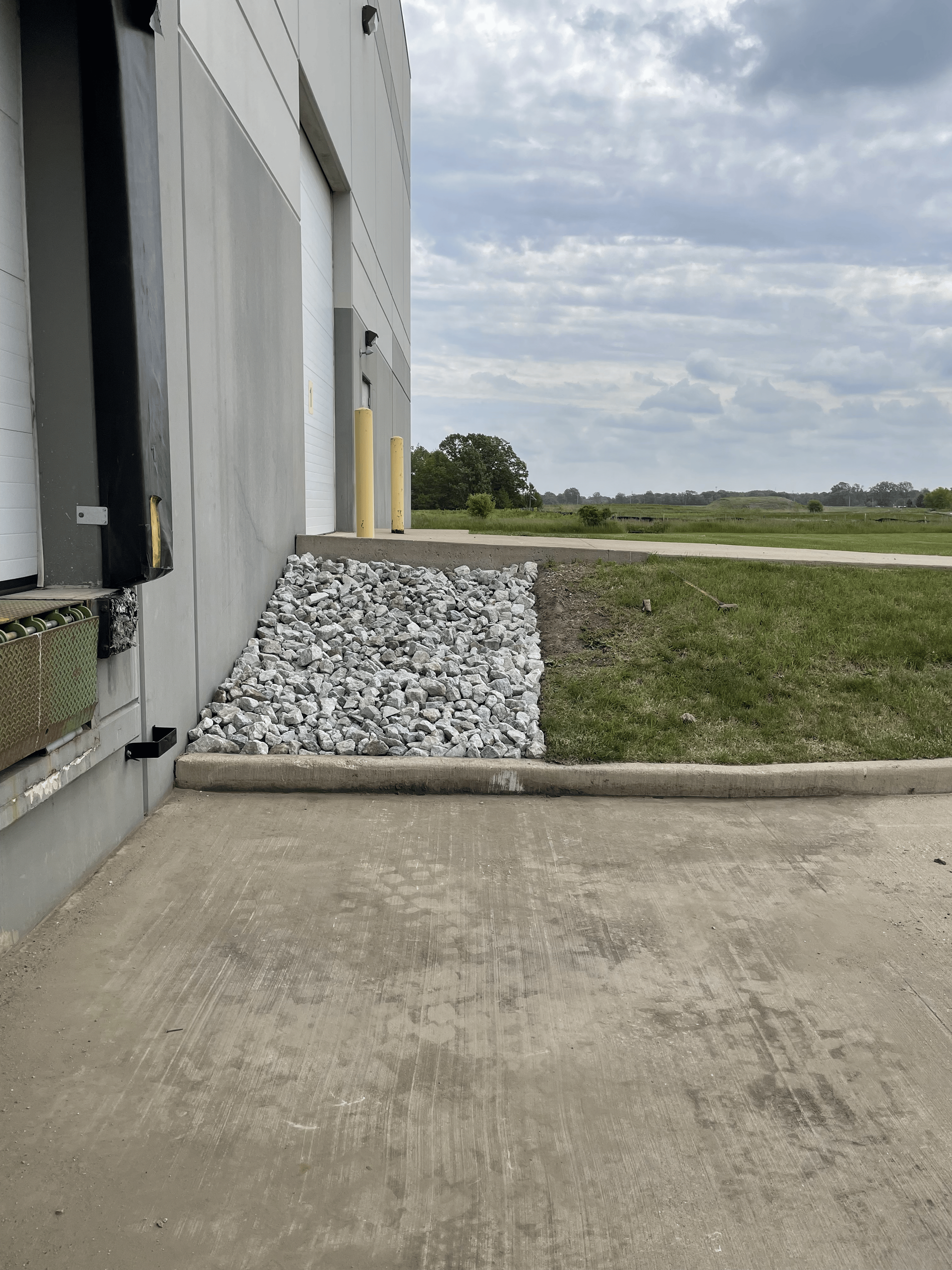 Loading dock exterior with concrete, rocks, and grass. Cloudy sky in the background.