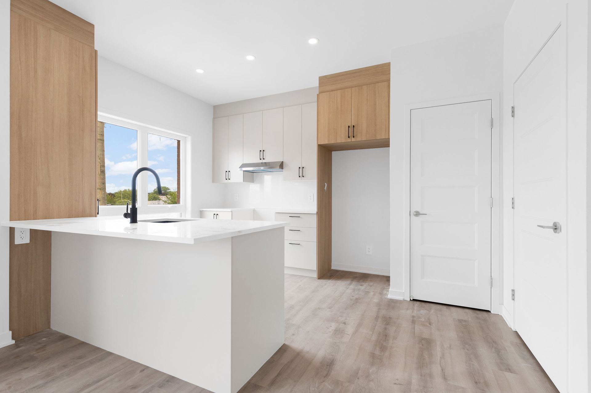 Cuisine blanche moderne avec armoires en bois, îlot et porte ouverte.