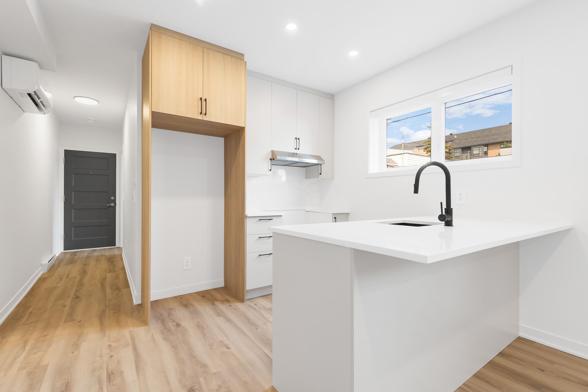 Cuisine blanche moderne avec îlot, armoires en bois et fenêtre.