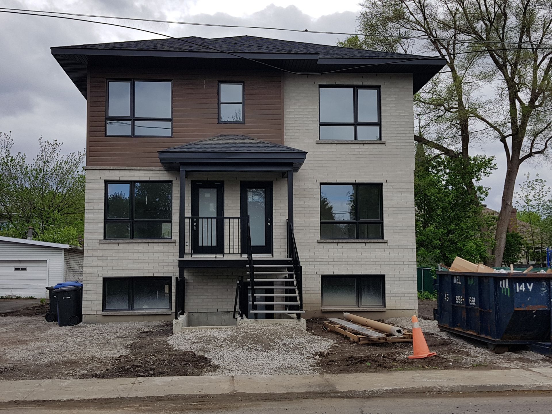 Duplex en brique et bois de deux étages avec fenêtres à cadre noir, porte d'entrée et escalier noir.