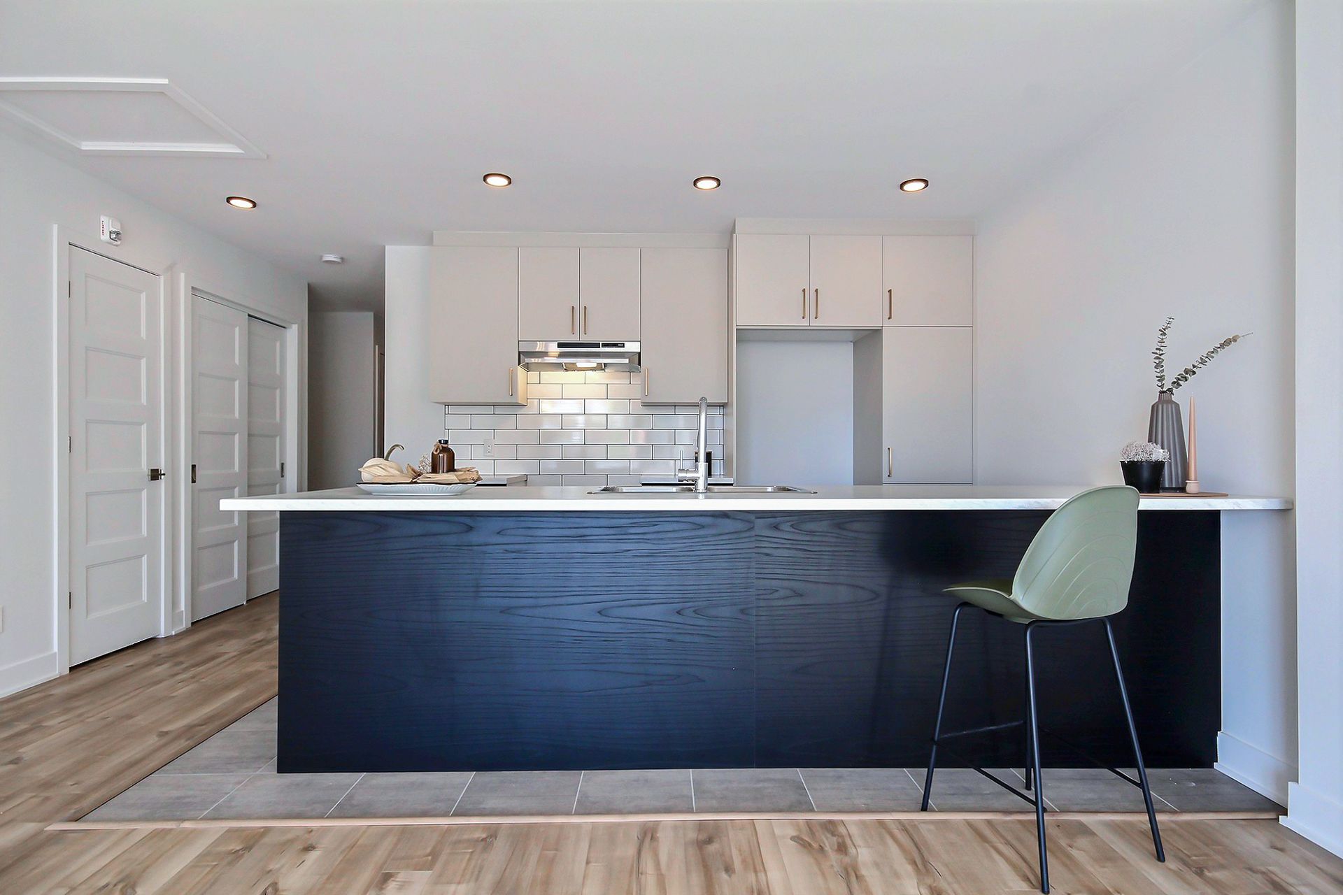 Cuisine moderne avec un îlot sombre, des armoires claires et un tabouret vert.