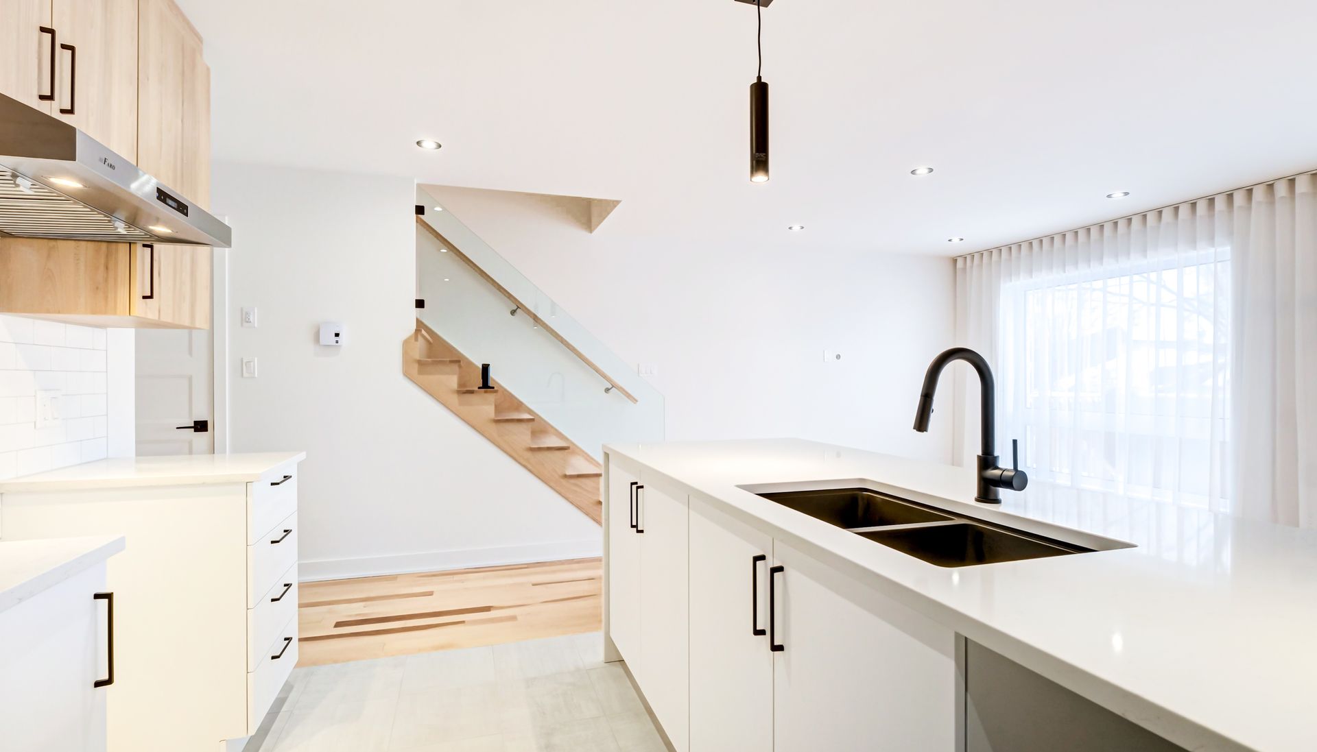 Cuisine moderne avec armoires blanches, îlot avec évier et escalier.