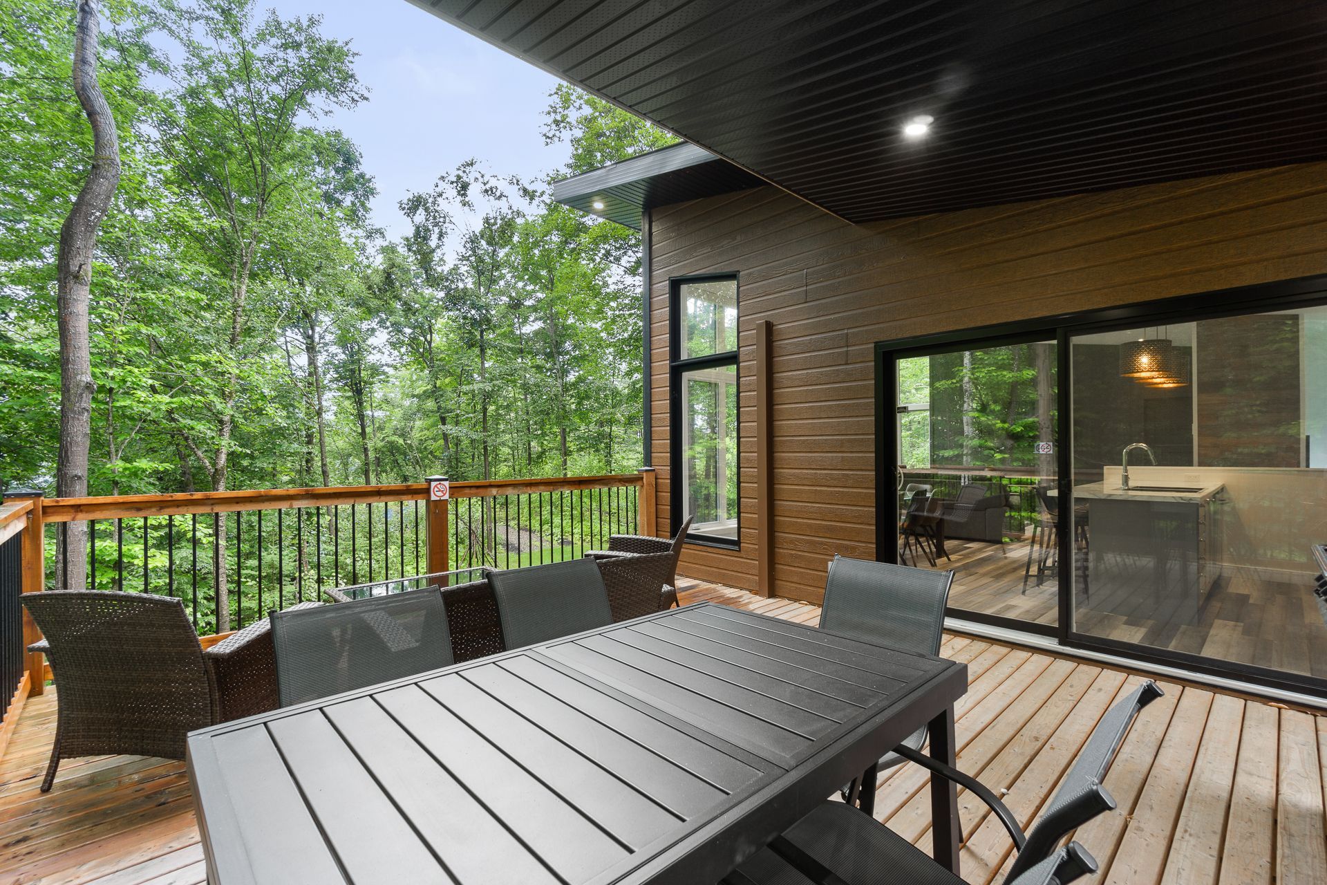 Terrasse avec table et chaises donnant sur la forêt. Une porte coulissante en verre mène à l'intérieur.