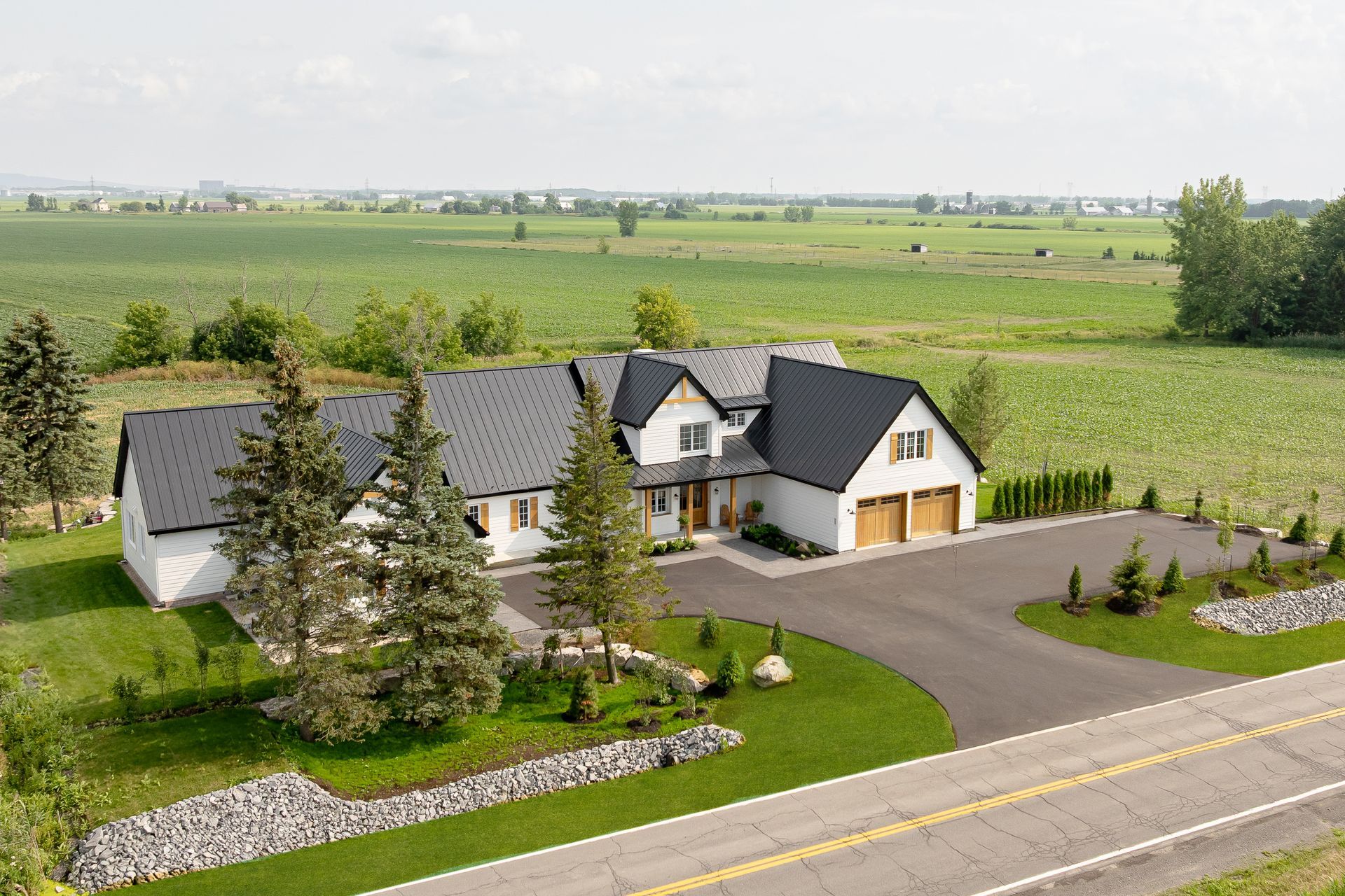 Maison blanche moderne avec toit noir et garage pour deux voitures située à côté d'un champ vert.
