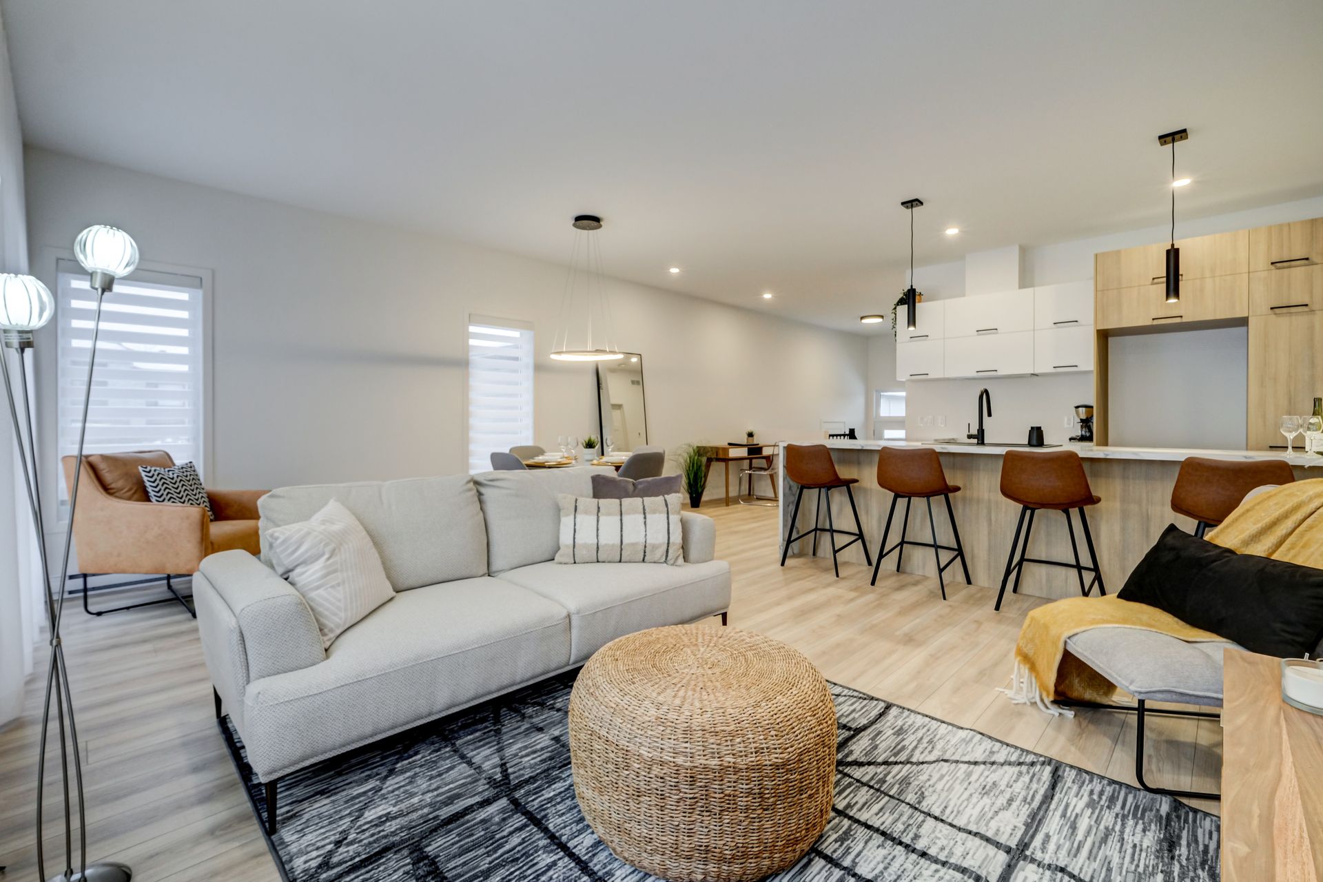 Salon moderne avec canapé, îlot de cuisine et tons neutres.
