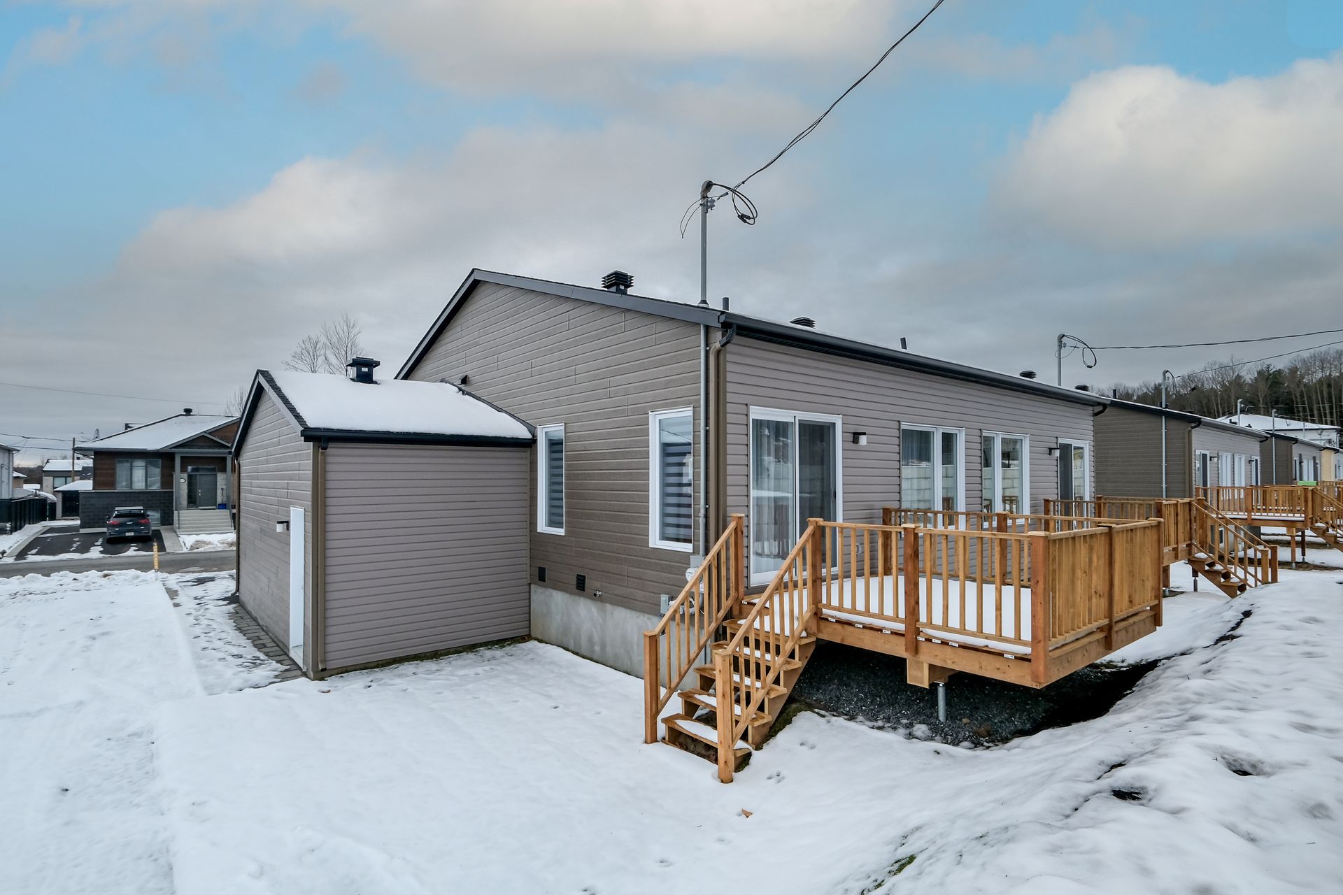 Une maison avec terrasse en bois et sol enneigé par temps nuageux.