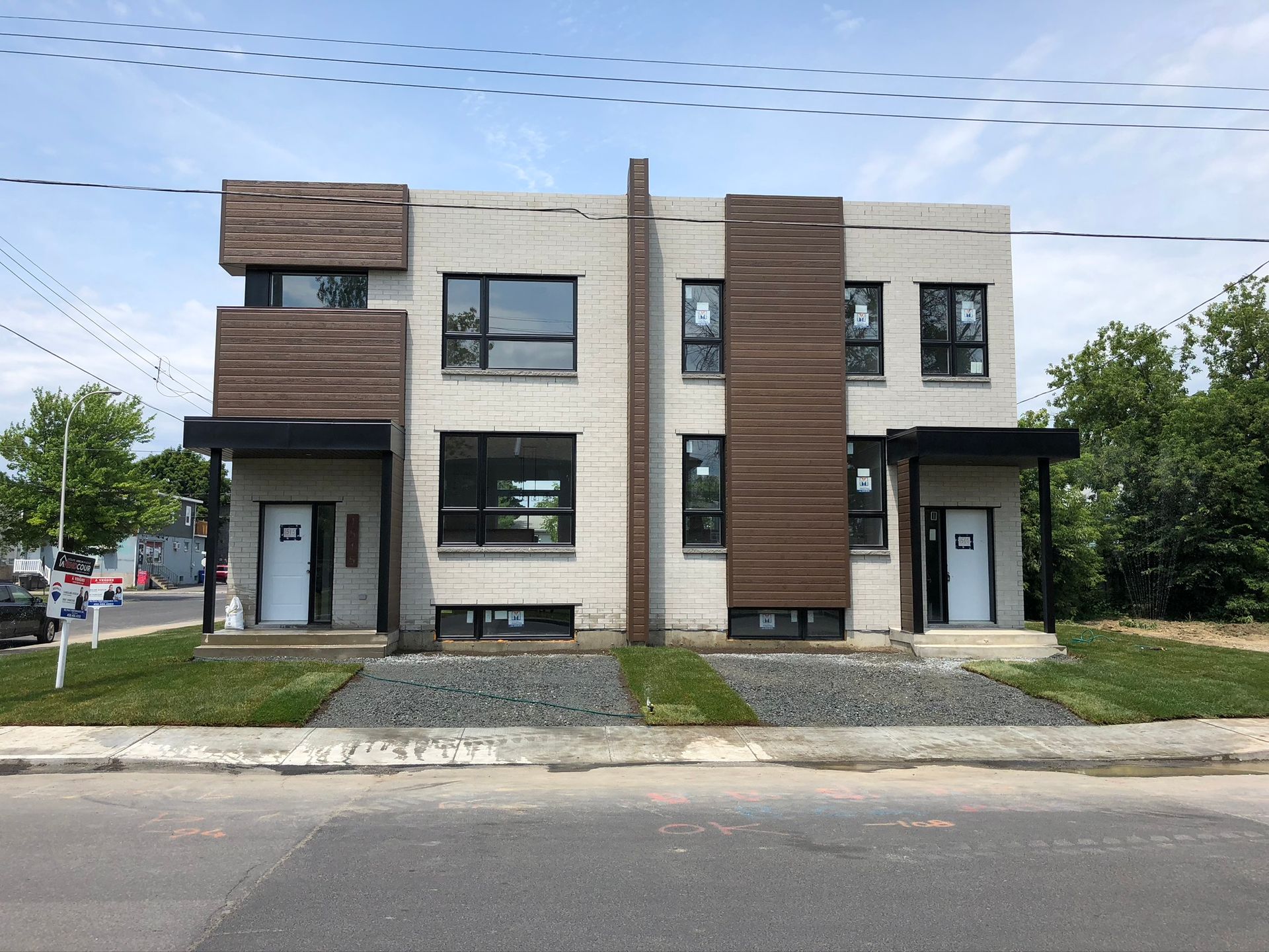 Bâtiment moderne en briques de deux unités avec des accents de bois foncé, chacune avec auvent et porte noirs.