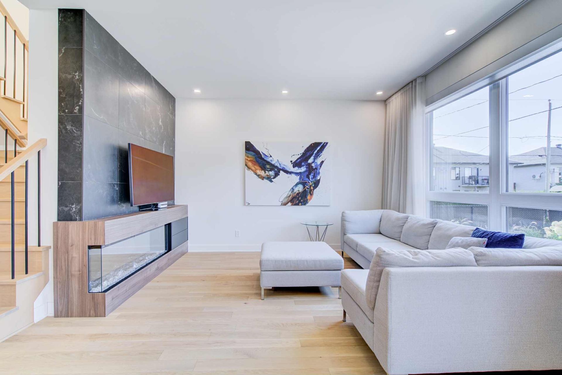 Salon moderne avec canapé gris, parquet en bois clair, grandes fenêtres et cheminée.