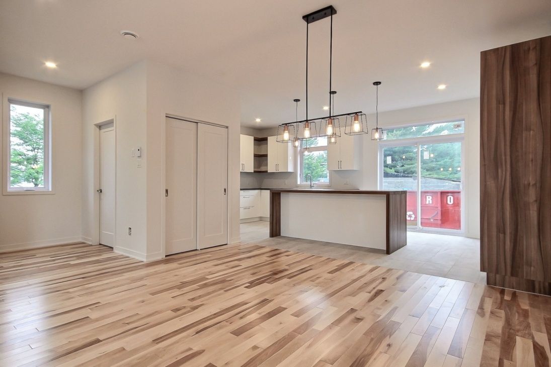 Espace de vie ouvert avec parquet, armoires blanches et îlot central en bois. Porte coulissante en verre à droite.
