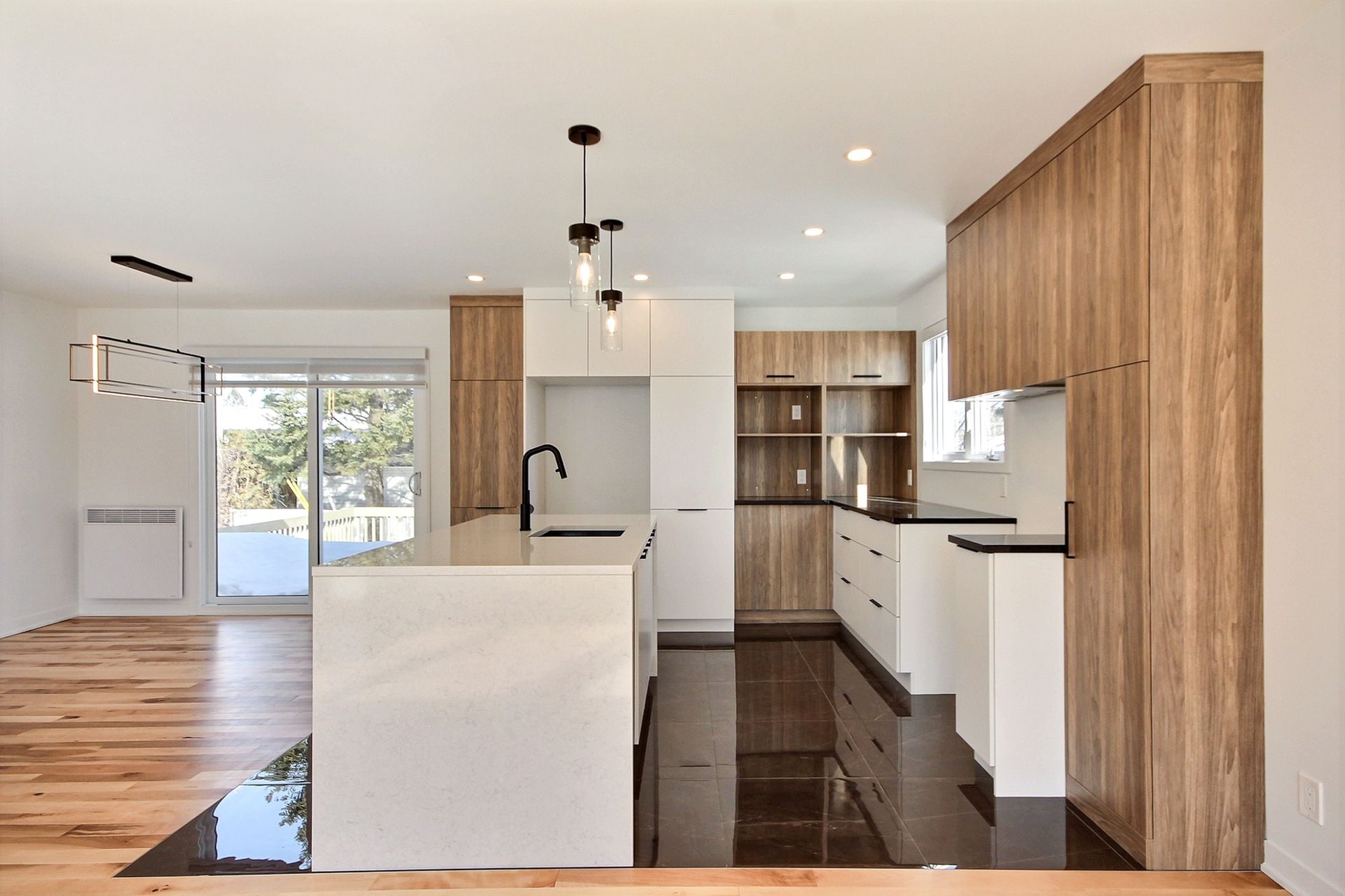 Cuisine moderne avec îlot blanc, plancher foncé, armoires en bois et luminaires suspendus.
