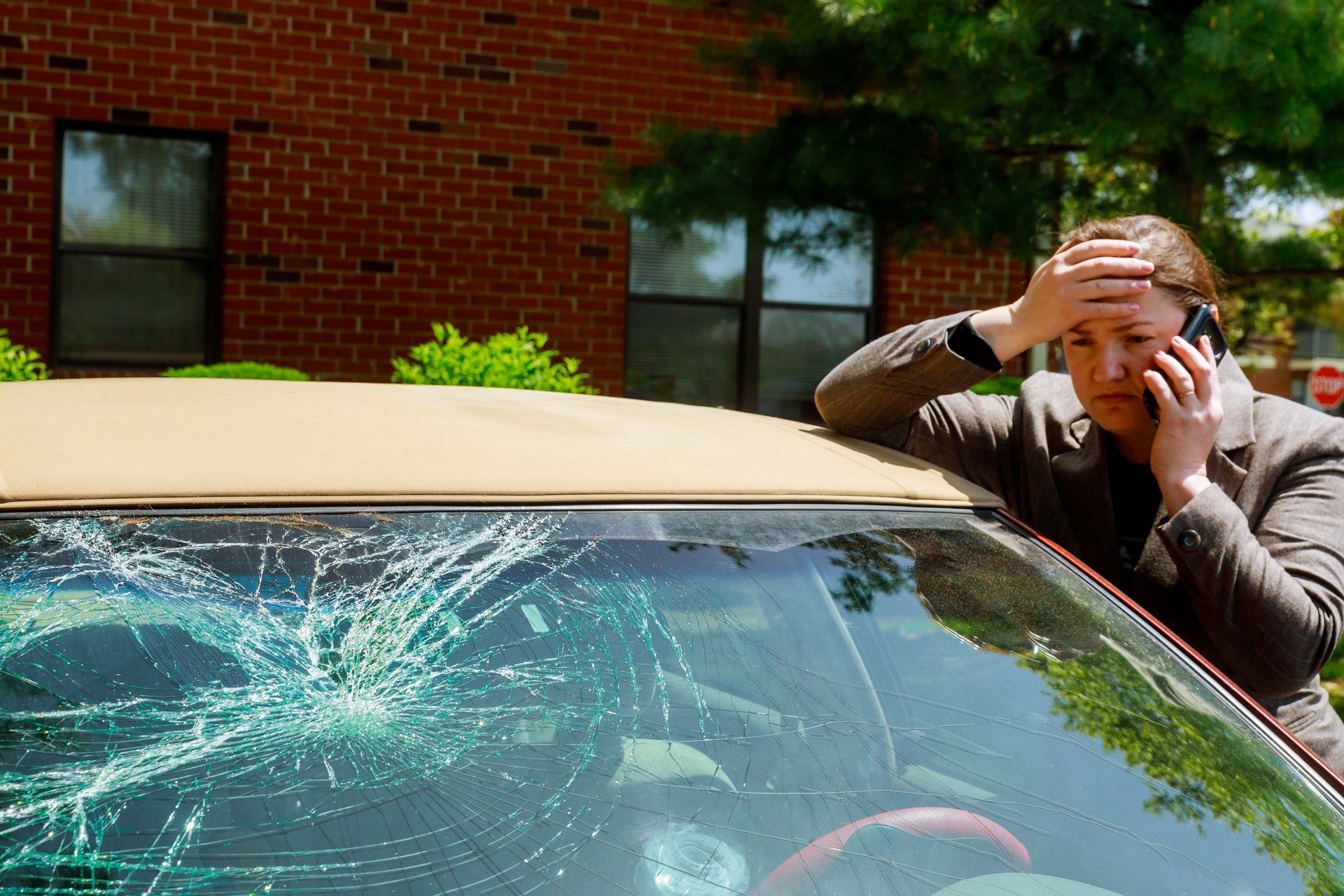 A woman is sitting in a car with a broken windshield talking on a cell phone.