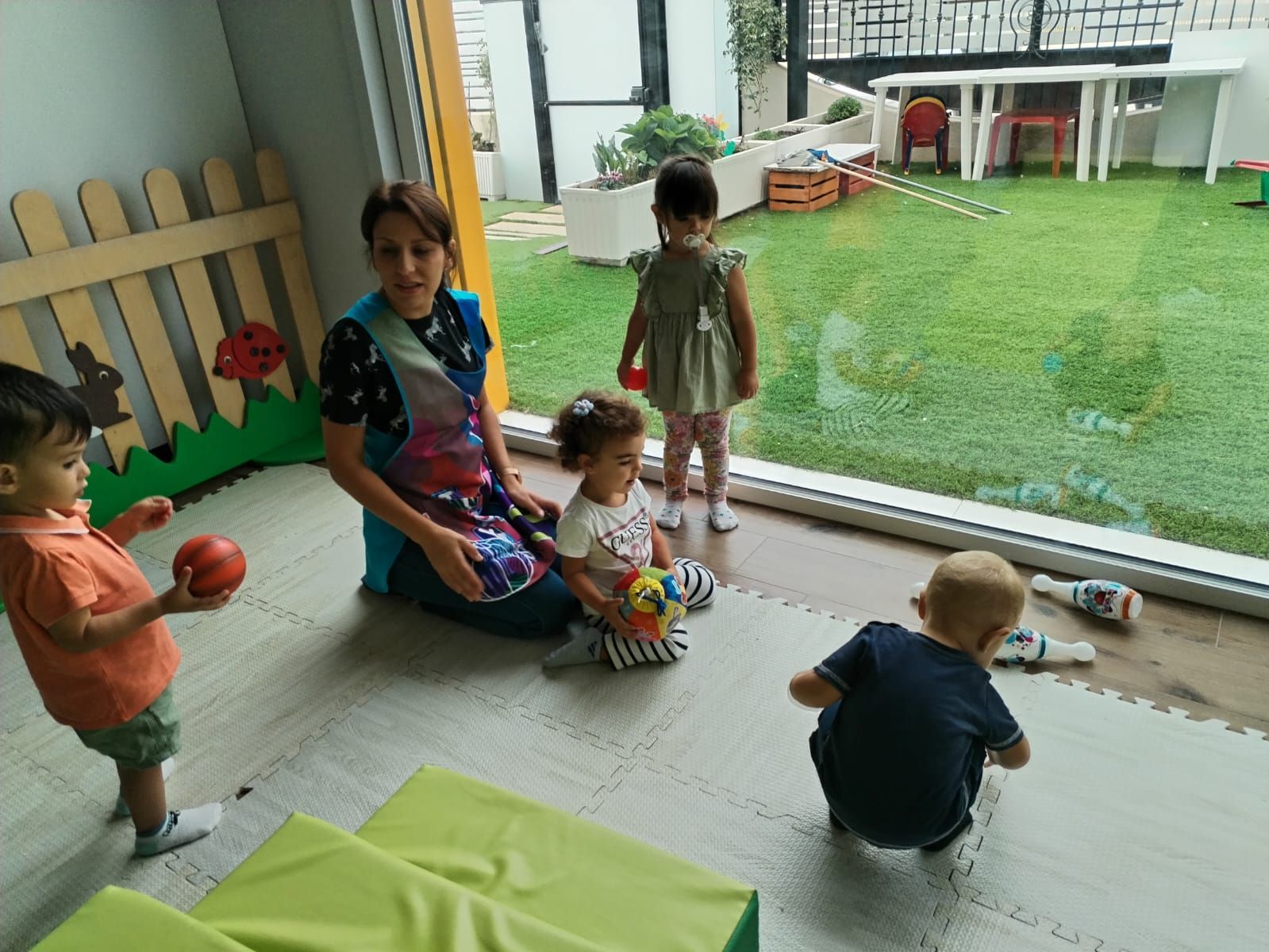 Un gruppo di bambini sta giocando in una stanza con una donna seduta sul pavimento.