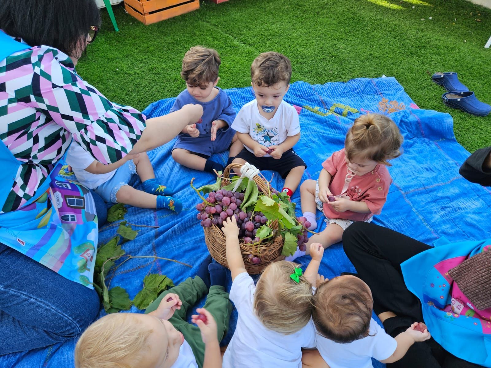 Un gruppo di bambini è seduto su un telo blu sull'erba.