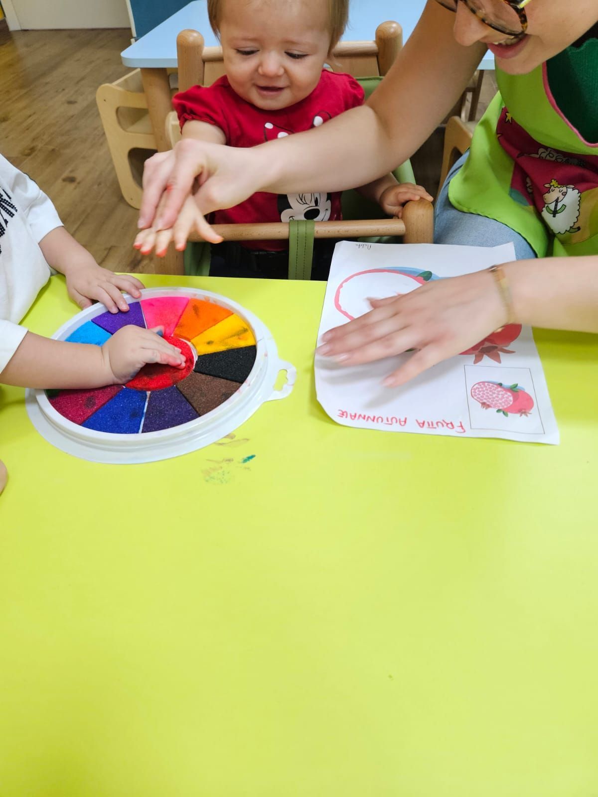 Una donna è seduta a un tavolo con due bambini che giocano con una ruota colorata.