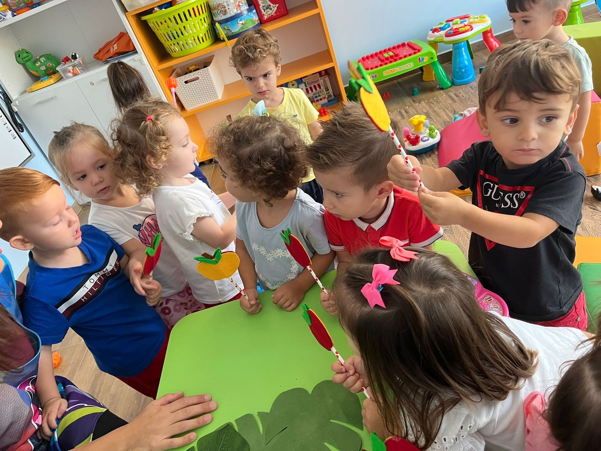 Un gruppo di bambini è seduto attorno a un tavolo e gioca con bastoncini e mele in feltro.