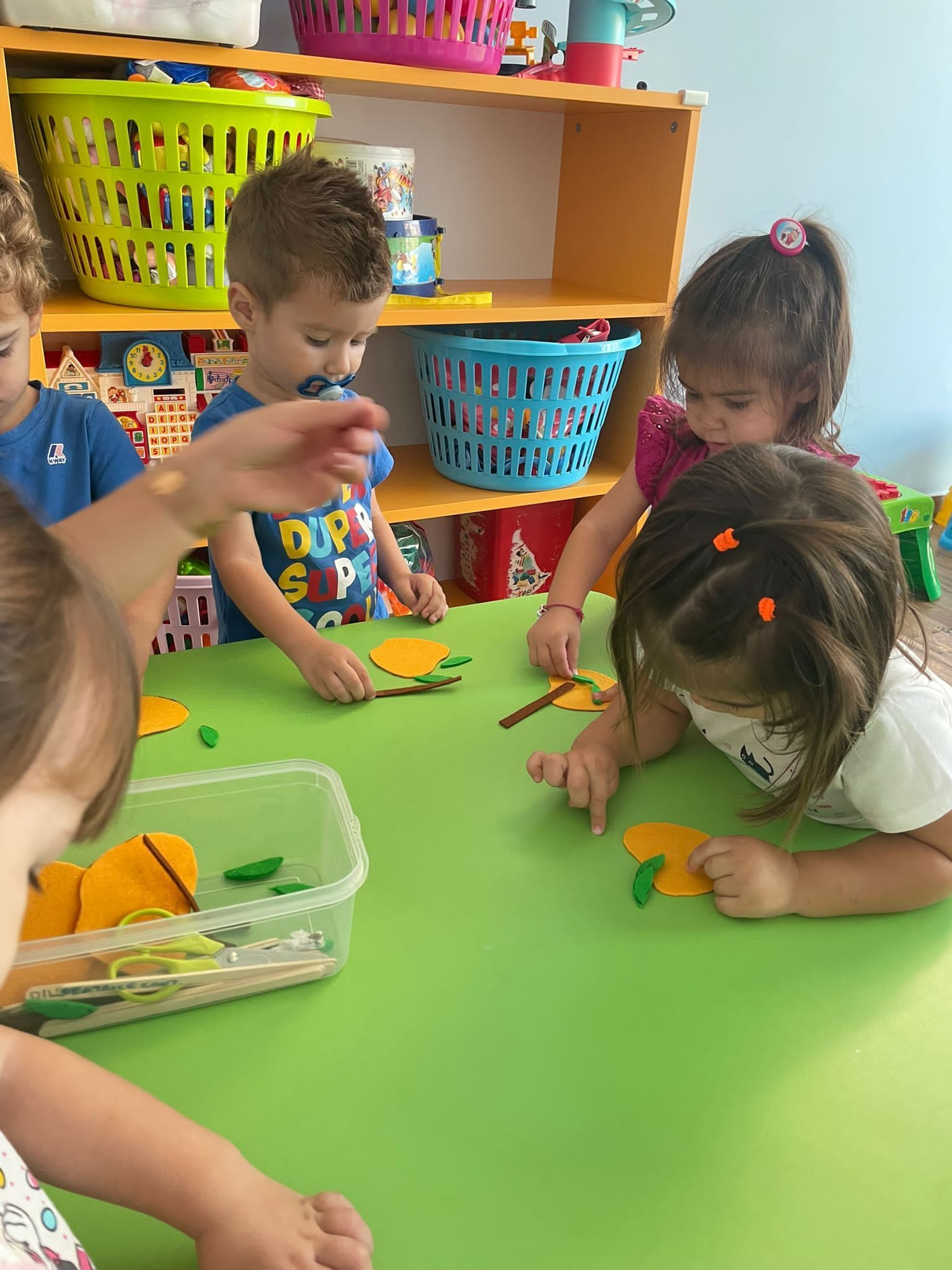 Un gruppo di bambini è seduto a un tavolo e gioca con mele di feltro.