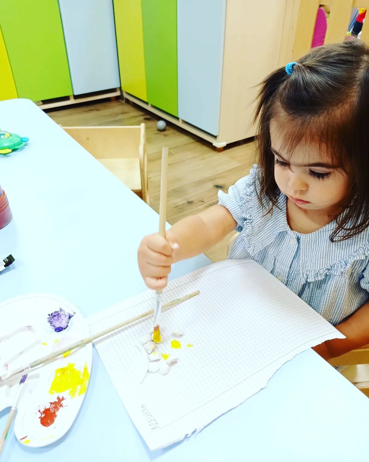 Una bambina è seduta a un tavolo e dipinge con un pennello