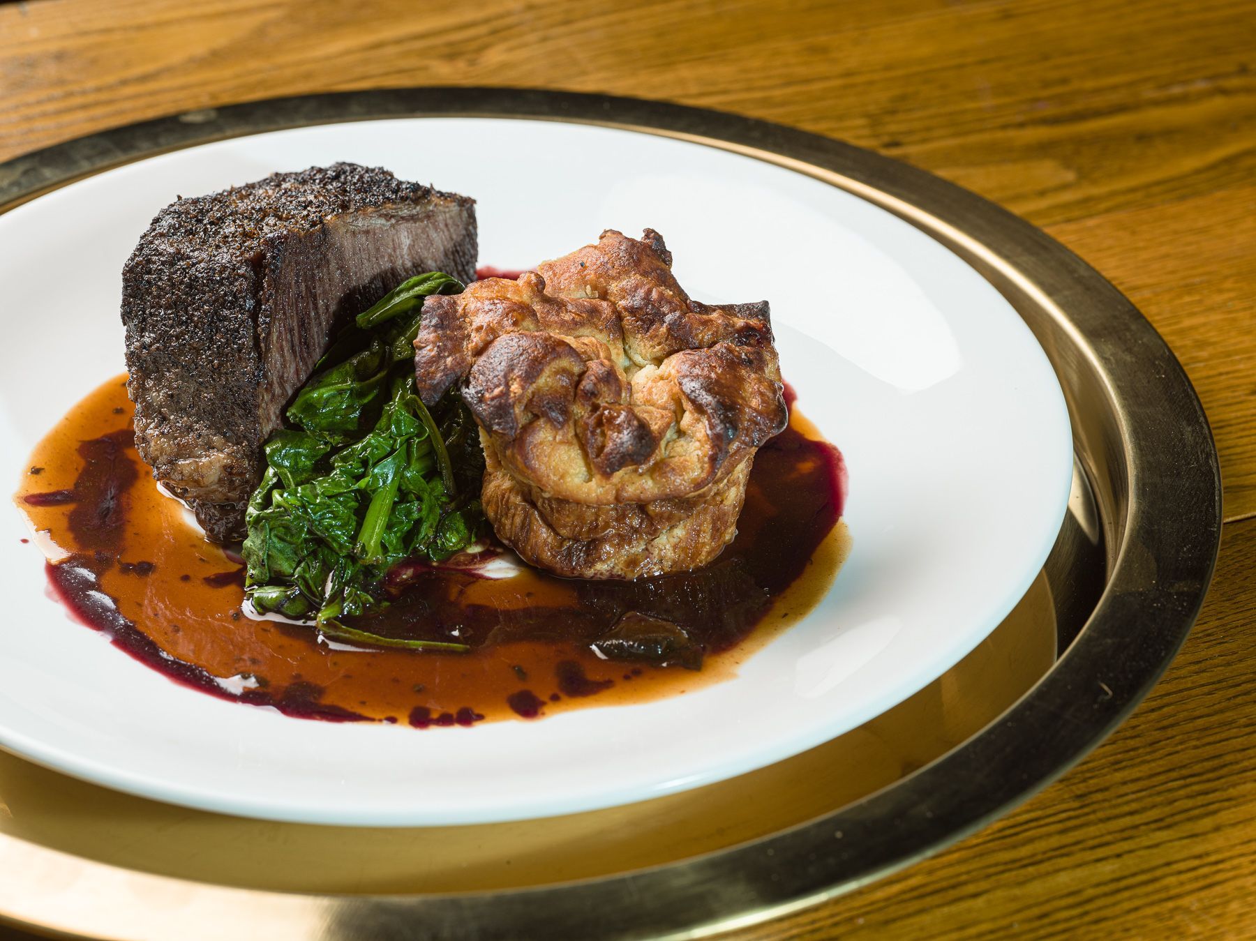 A white plate topped with meat and sauce on a wooden table