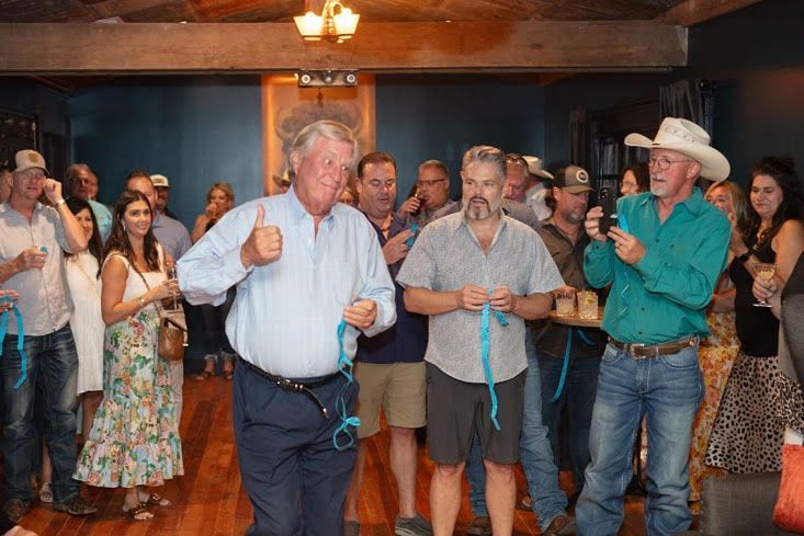 A group of people are standing around a man in a cowboy hat giving a thumbs up.