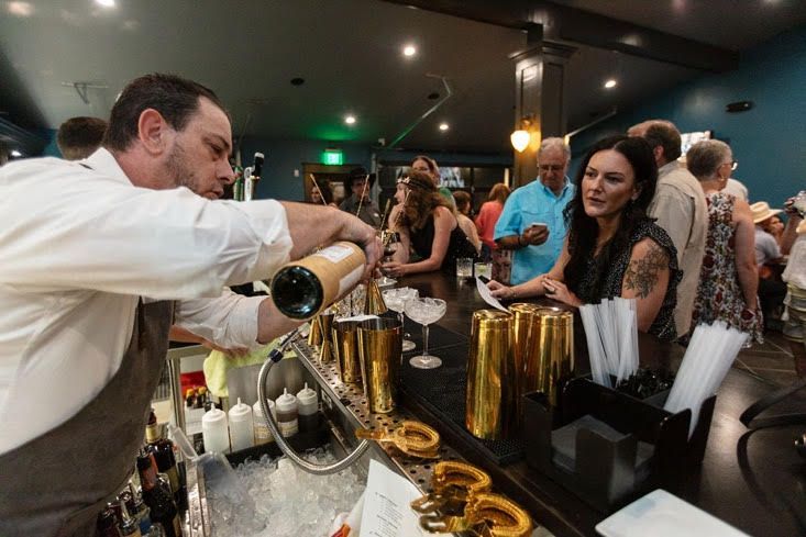 A man is pouring champagne into a glass at a bar.