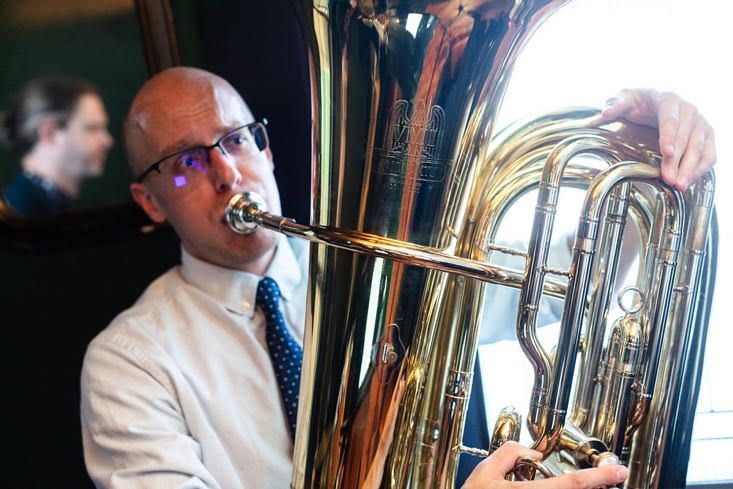 A man in a white shirt and tie is playing a tuba.
