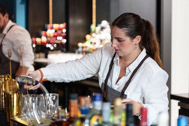 A woman is pouring a drink into a glass at a bar.